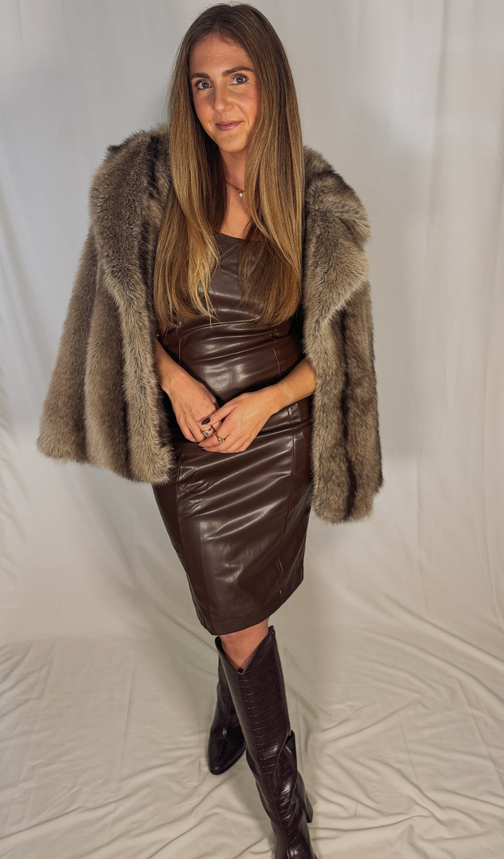 Woman wearing a brown fur coat, leather skirt, and boots on a plain background