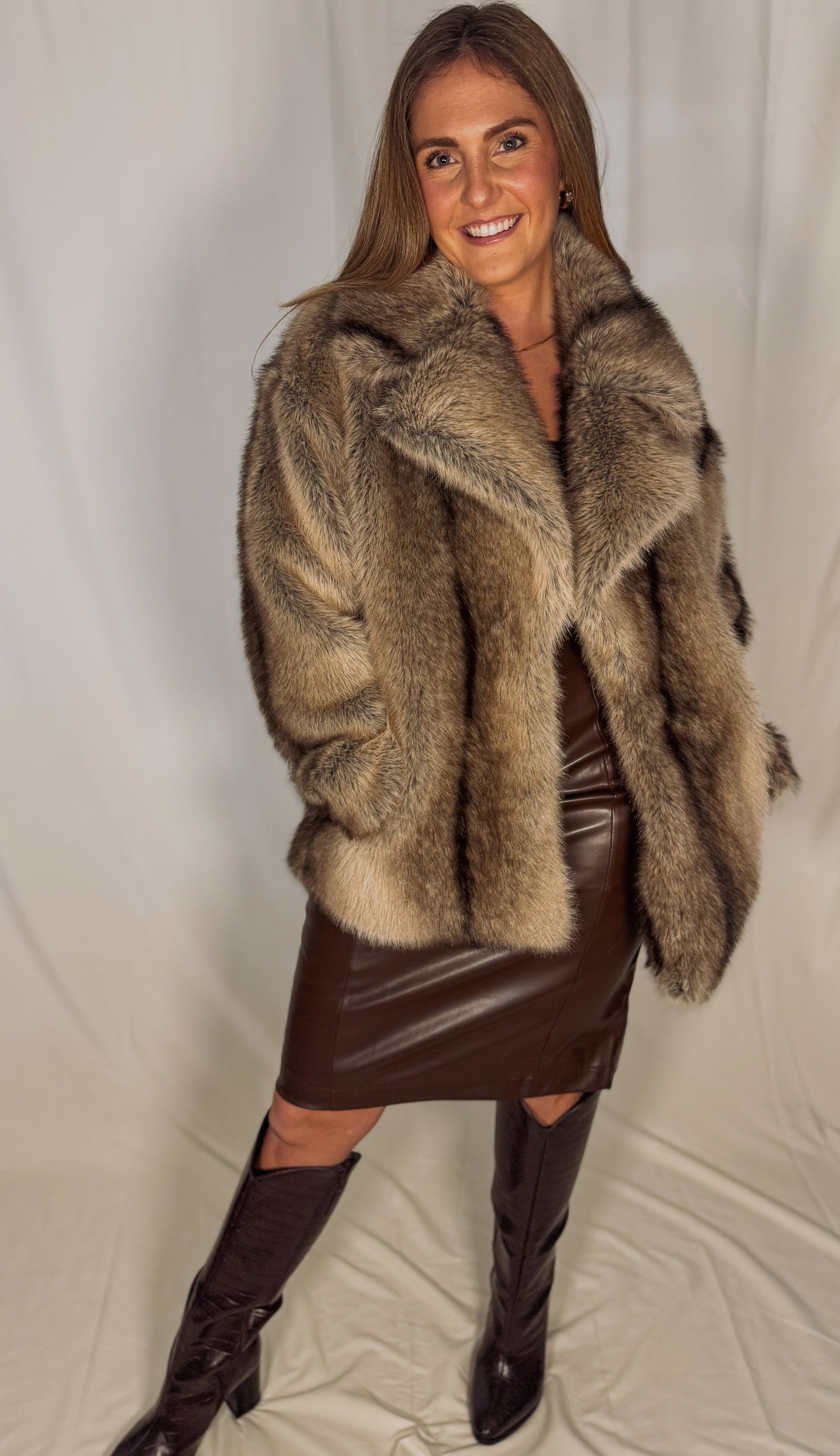 Woman wearing a fur coat and leather skirt against a plain background