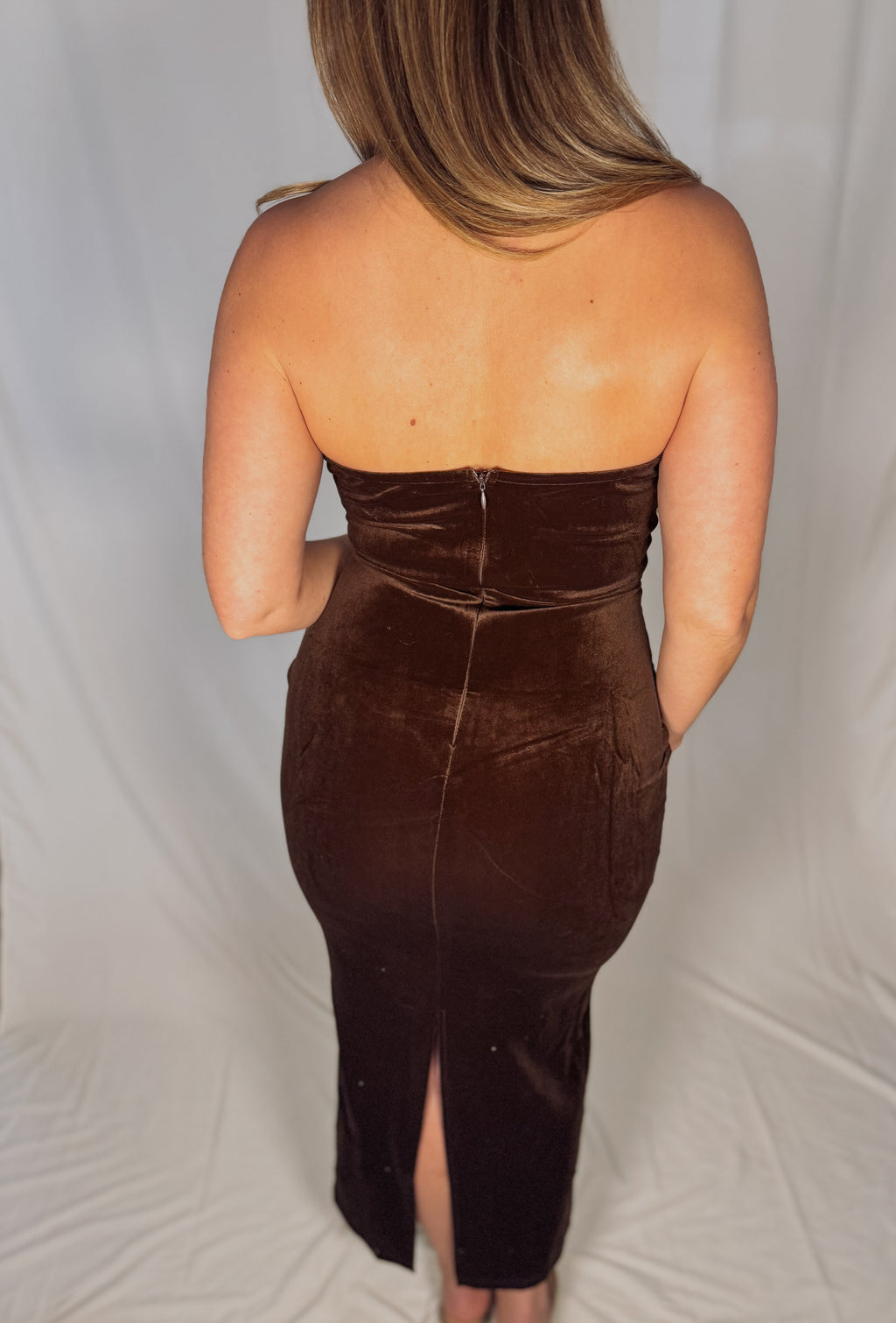 Brown strapless dress with a slit on a plain background