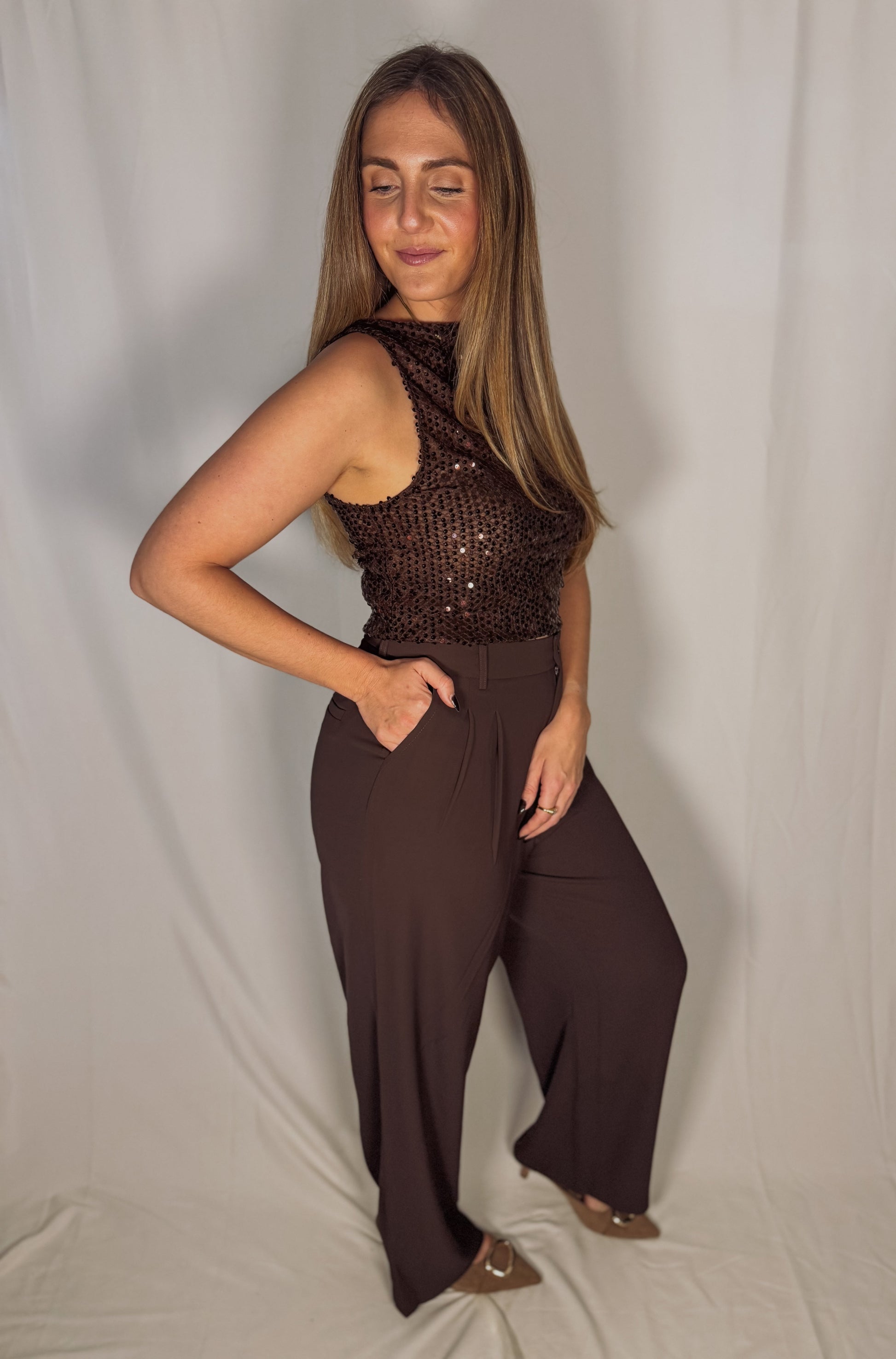Woman wearing a brown sequined top and wide-leg pants against a plain background