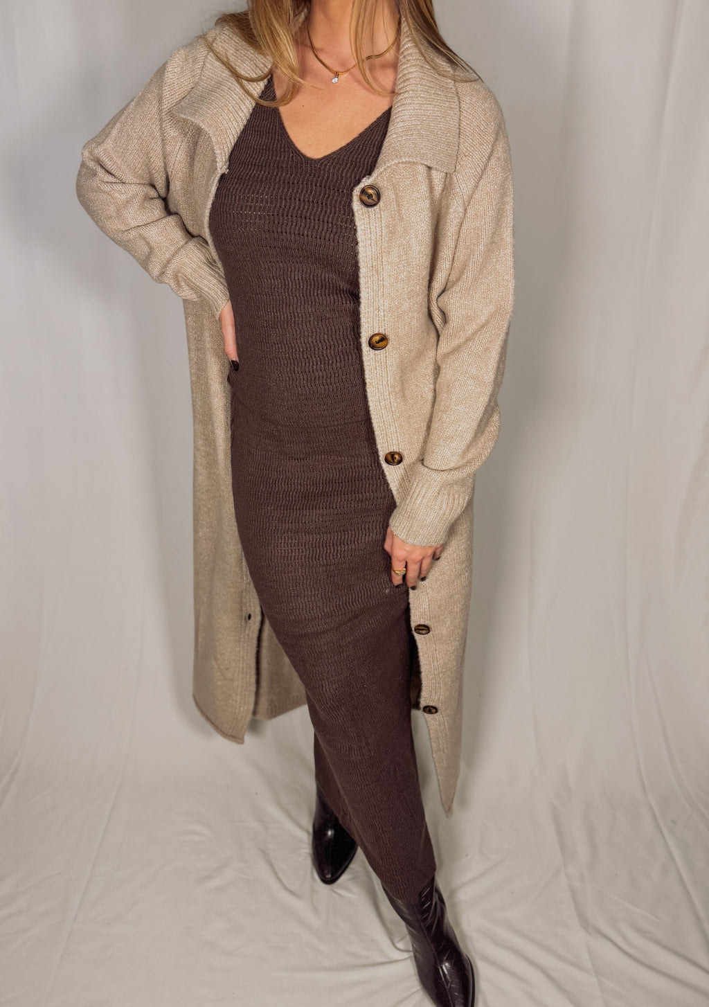 Person wearing a long beige cardigan over a brown dress on a white background