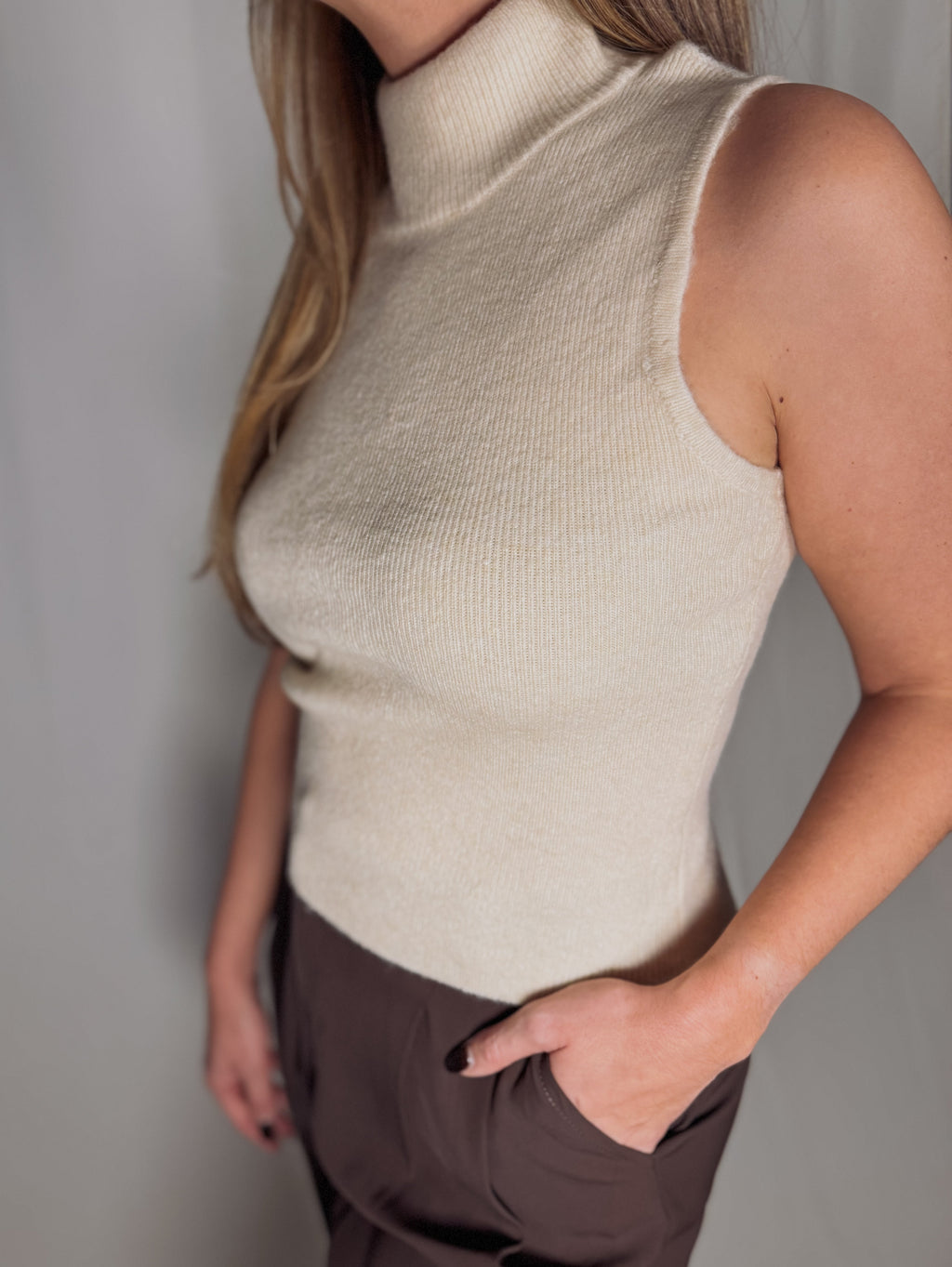 Person wearing a beige sleeveless knit top against a plain background