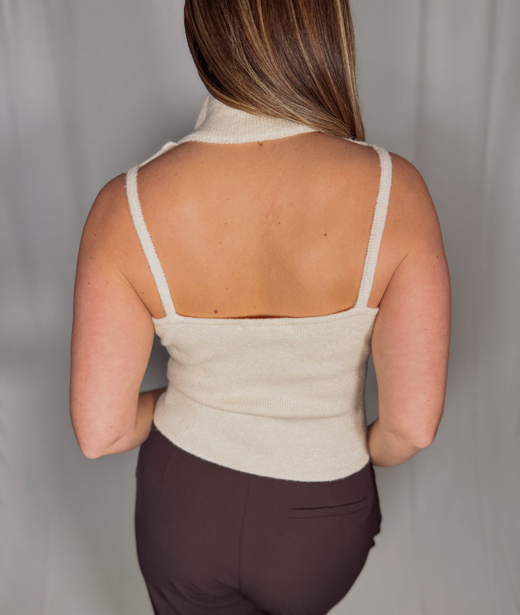 Person wearing a beige sleeveless top with thin straps against a plain background