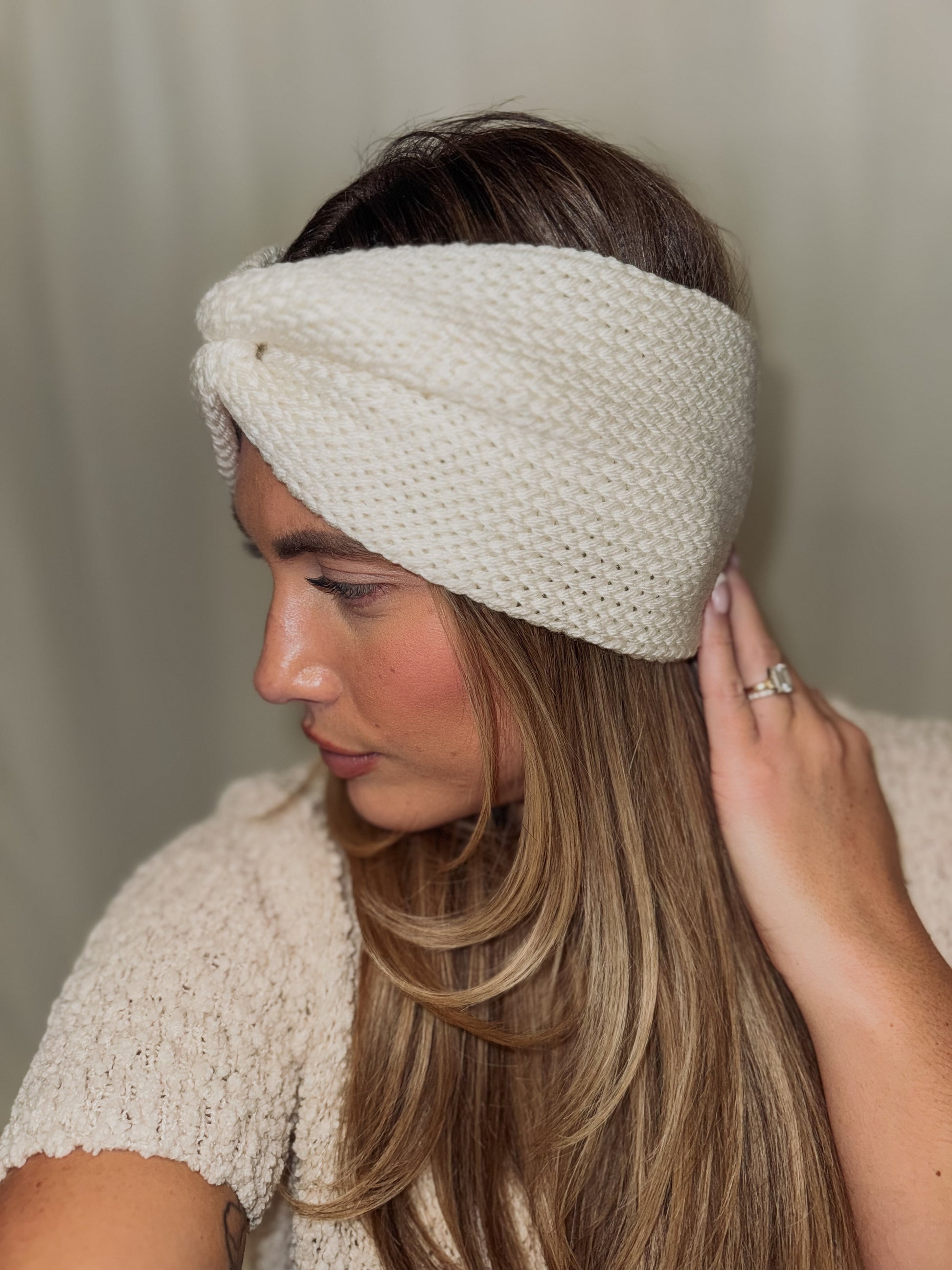 Woman wearing a white knitted headband against a neutral background