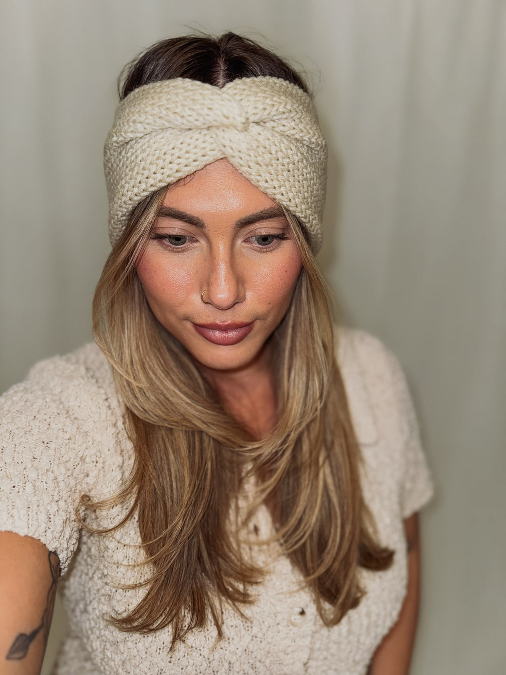 Woman wearing a beige knitted headband against a plain background