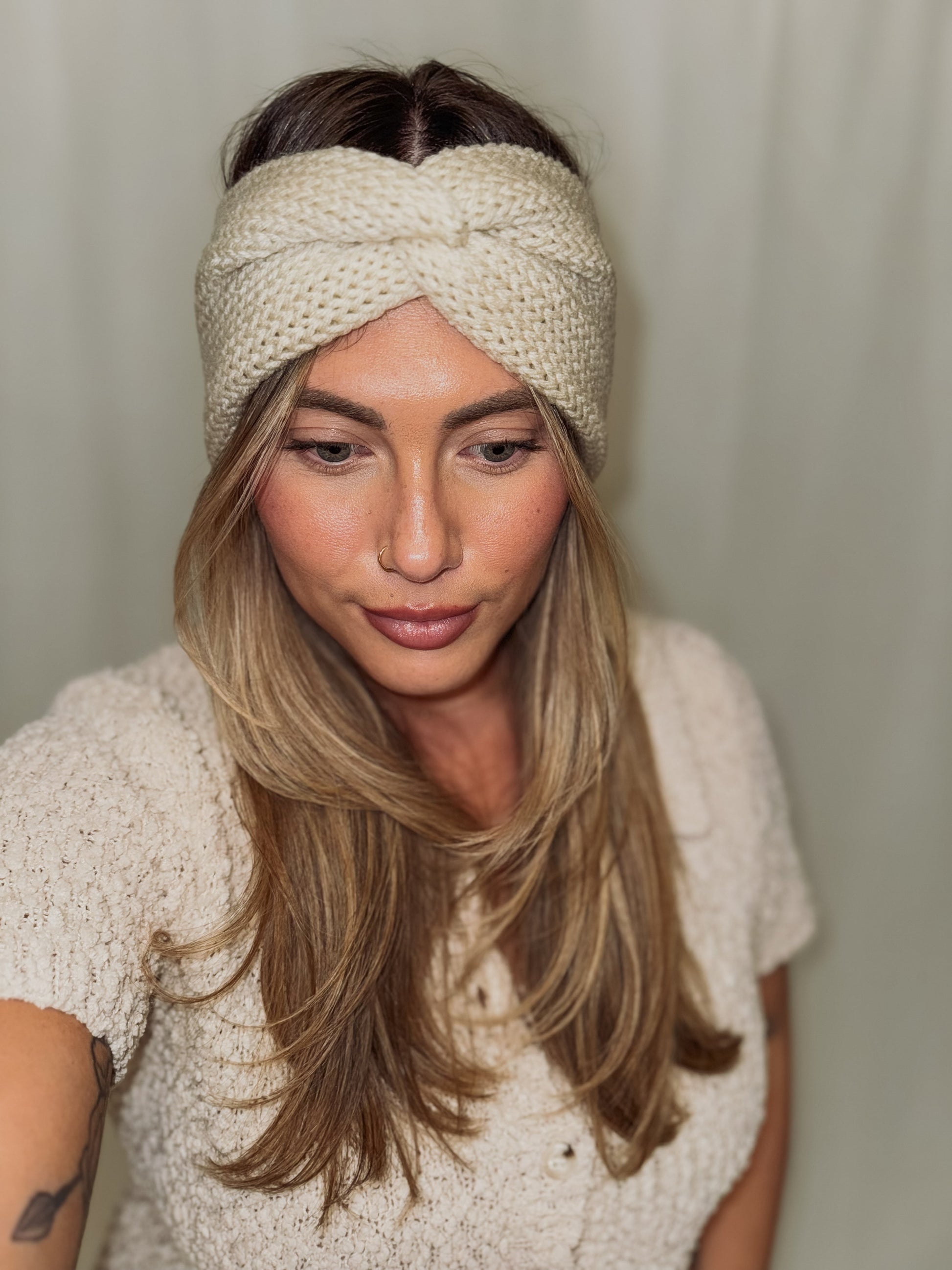 Woman wearing a beige knitted headband against a plain background