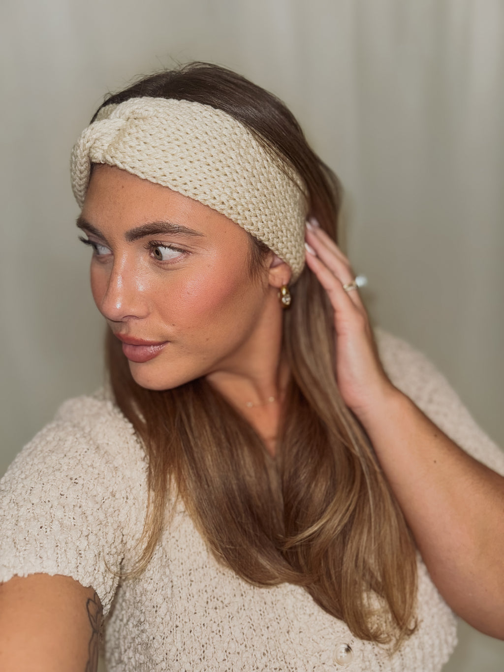 Woman wearing a beige knitted headband against a neutral background