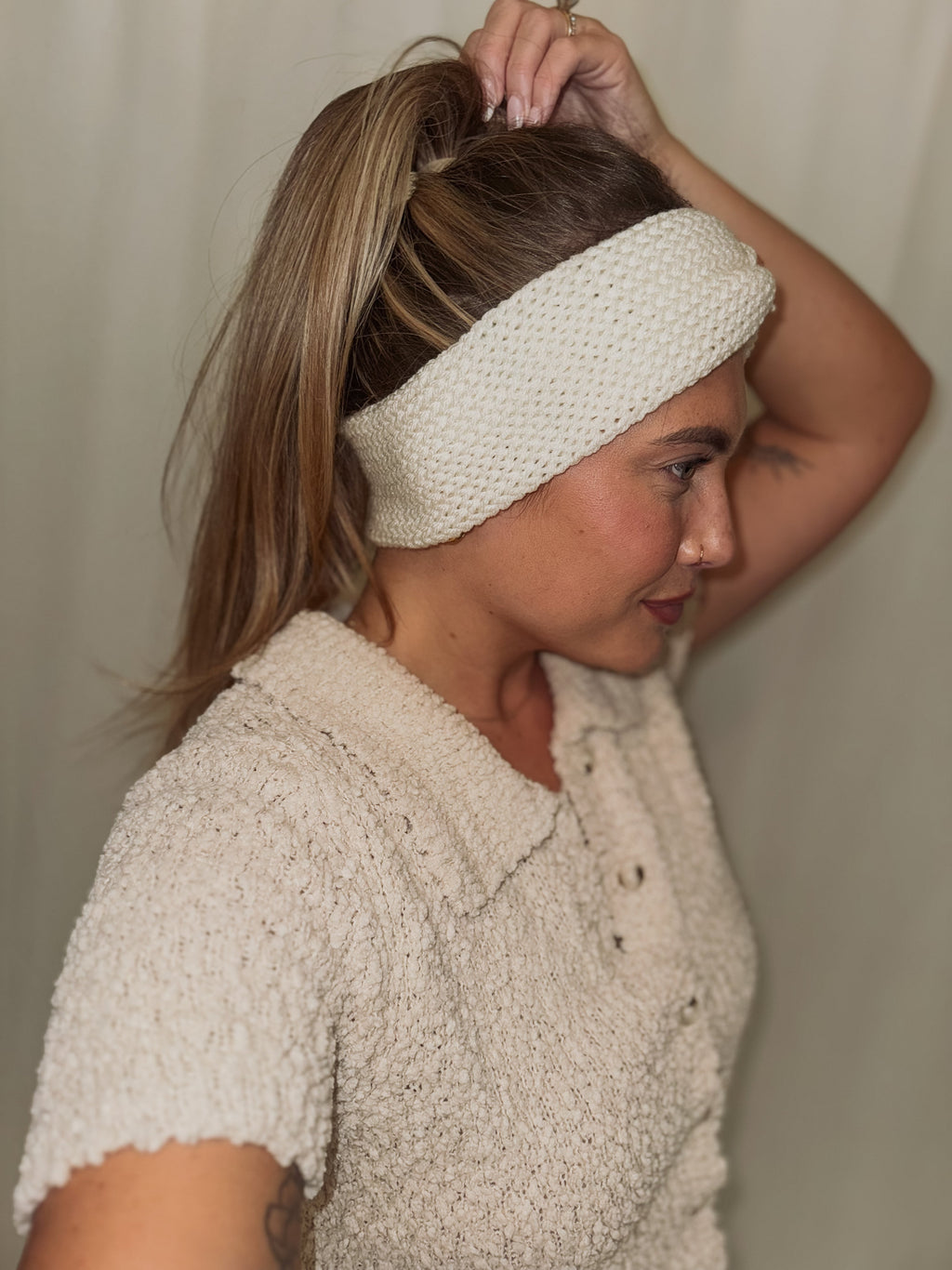 Woman wearing a white knitted headband against a plain background