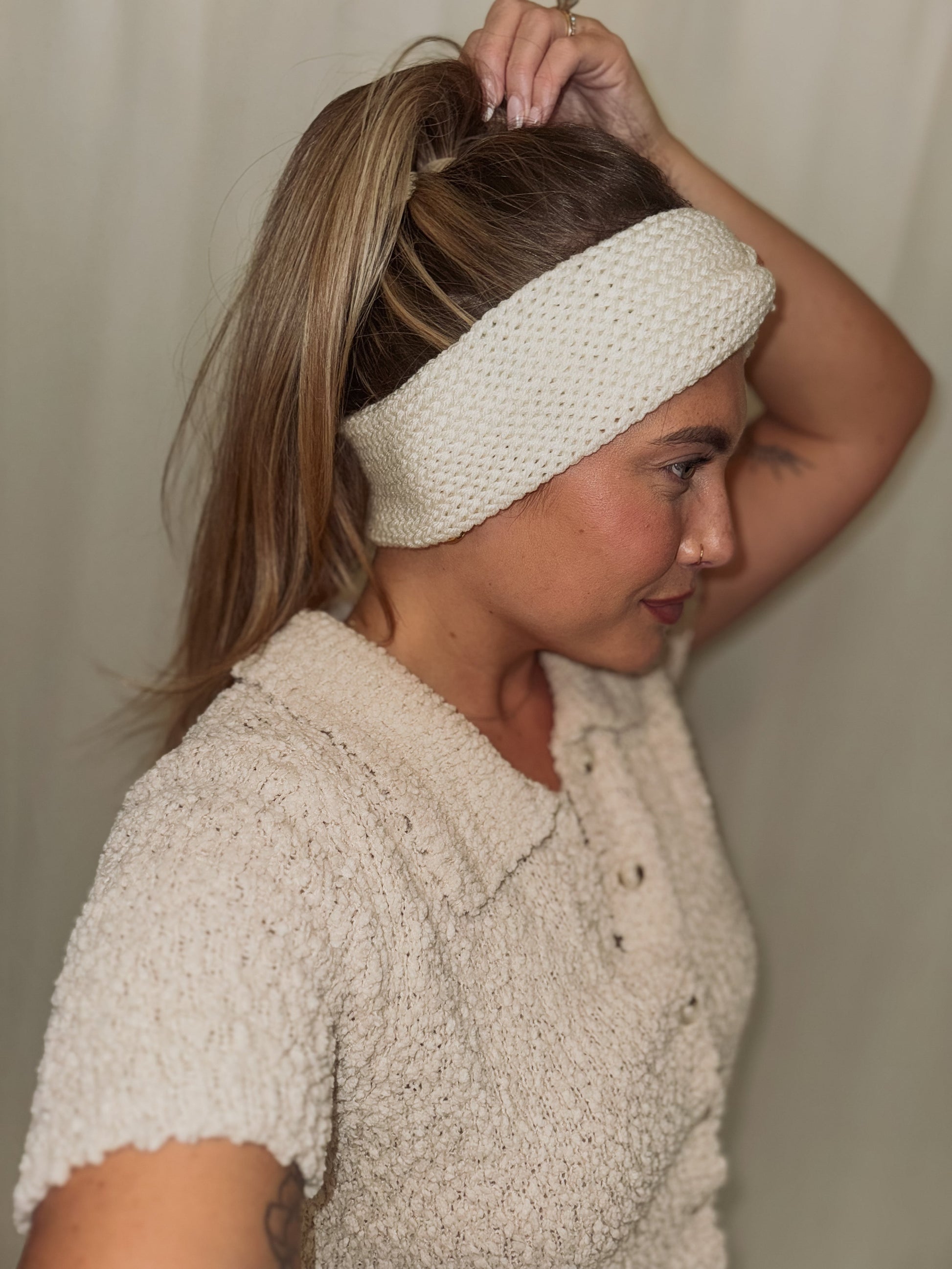 Woman wearing a white knitted headband against a plain background