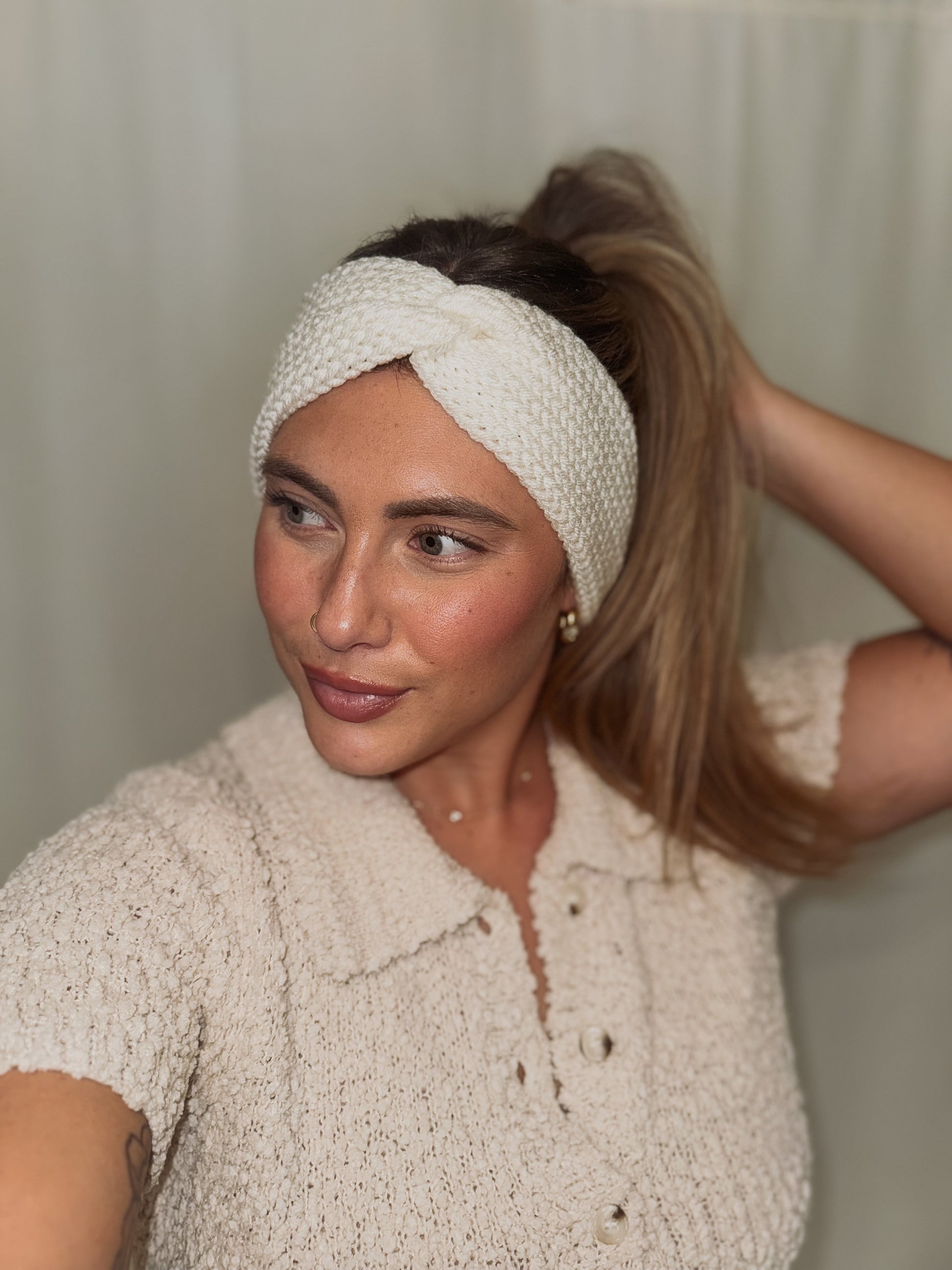 Woman wearing a white knitted headband against a neutral background