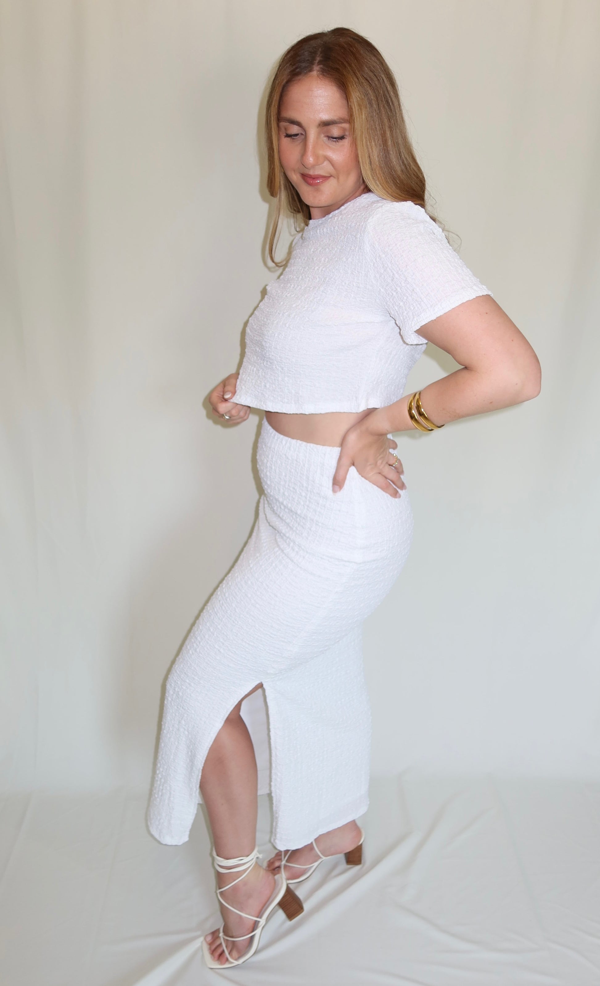 Person wearing a white textured top and skirt set on a plain background