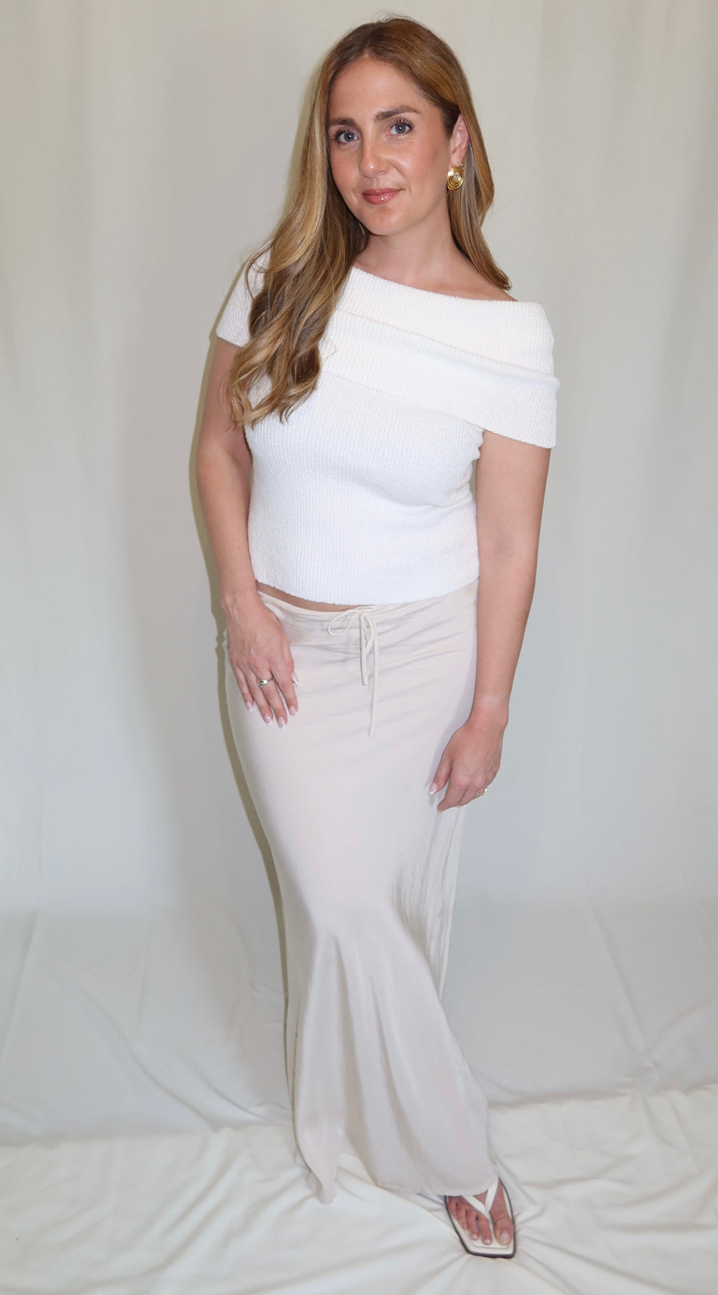 Woman in white knit off the shoulder top and cream satin skirt.
