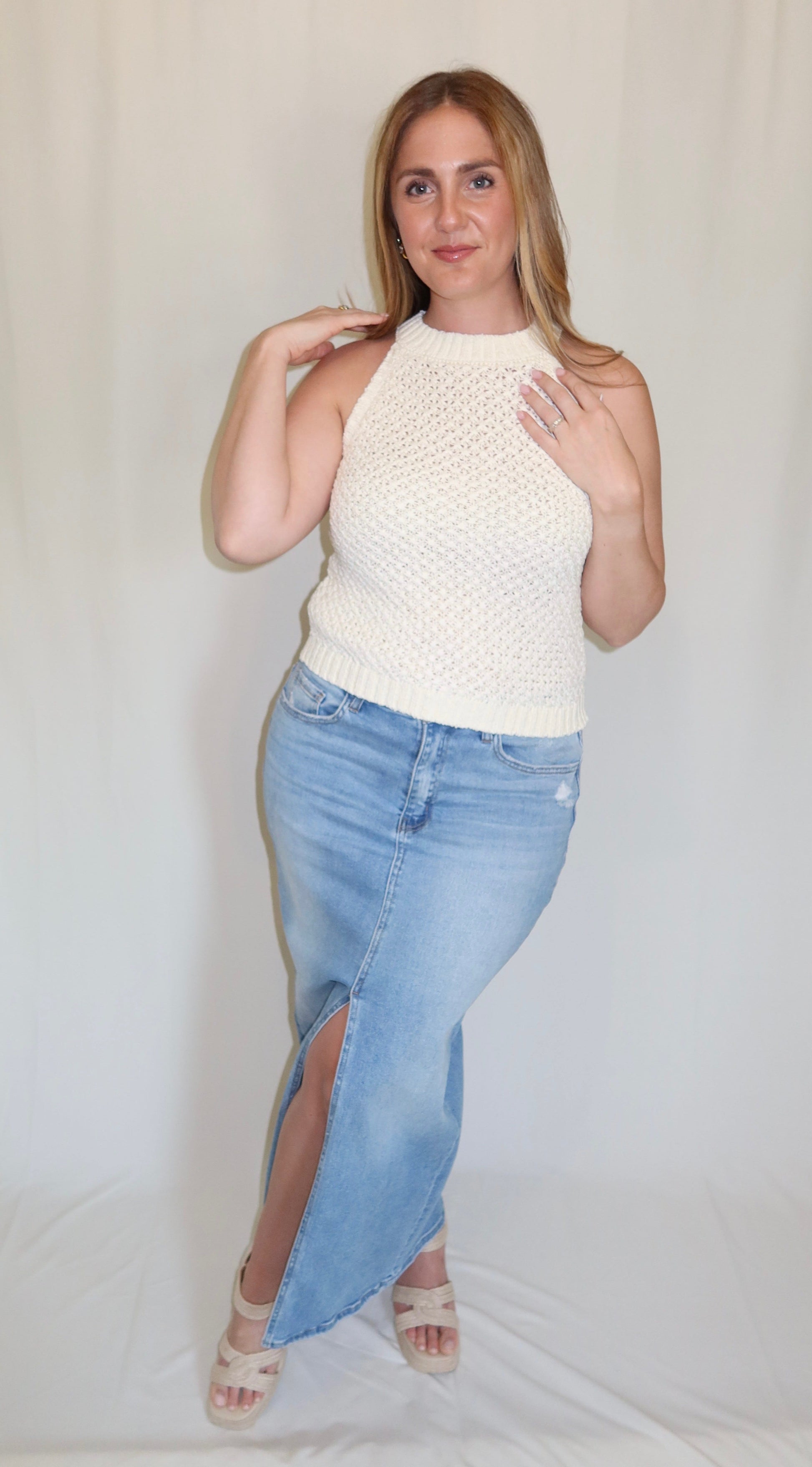 Woman wearing a white sleeveless top and light blue denim skirt on a plain background