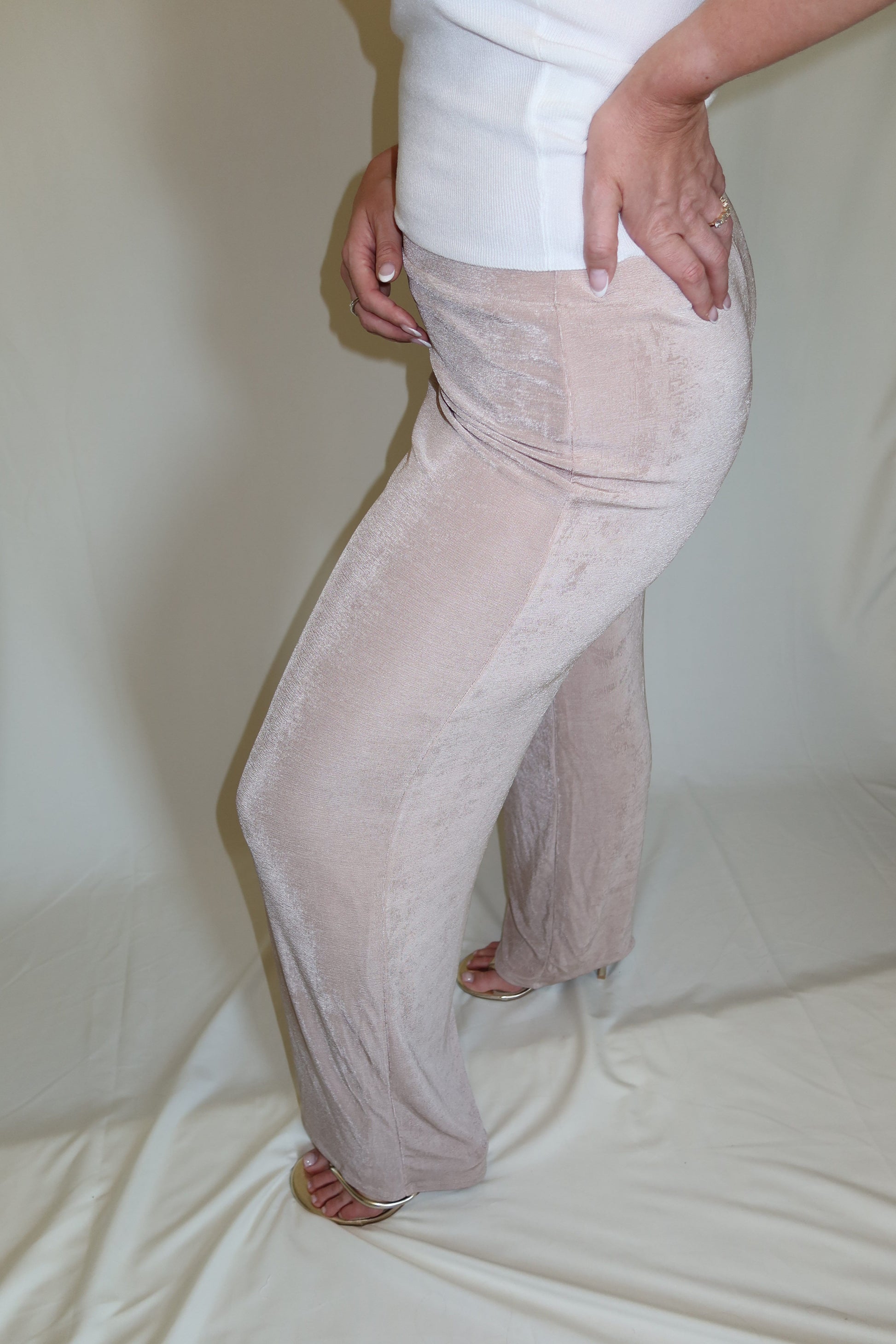 Person wearing beige pants and a white top on a plain background