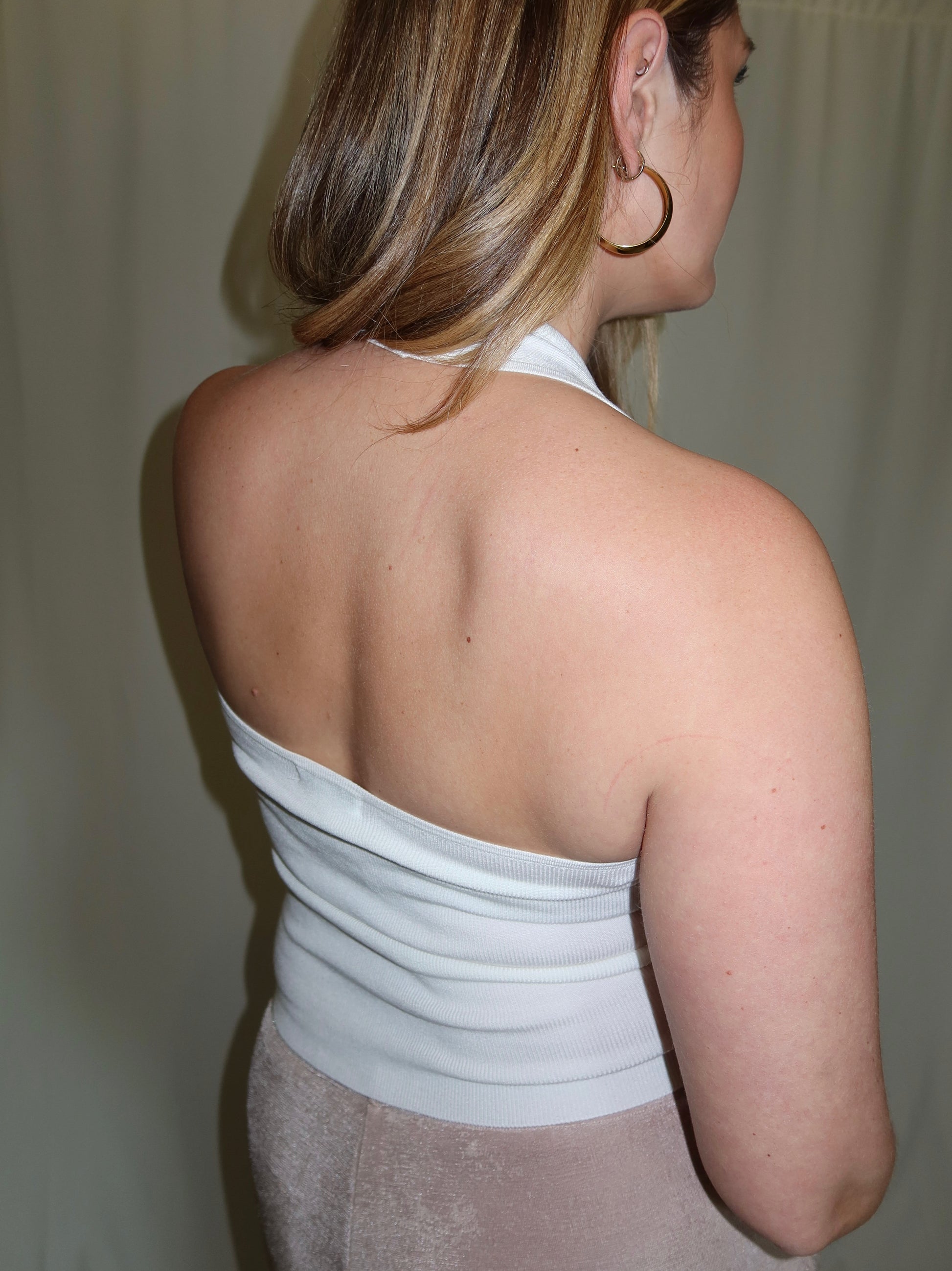 Woman wearing a white halter top with thin straps, back view.