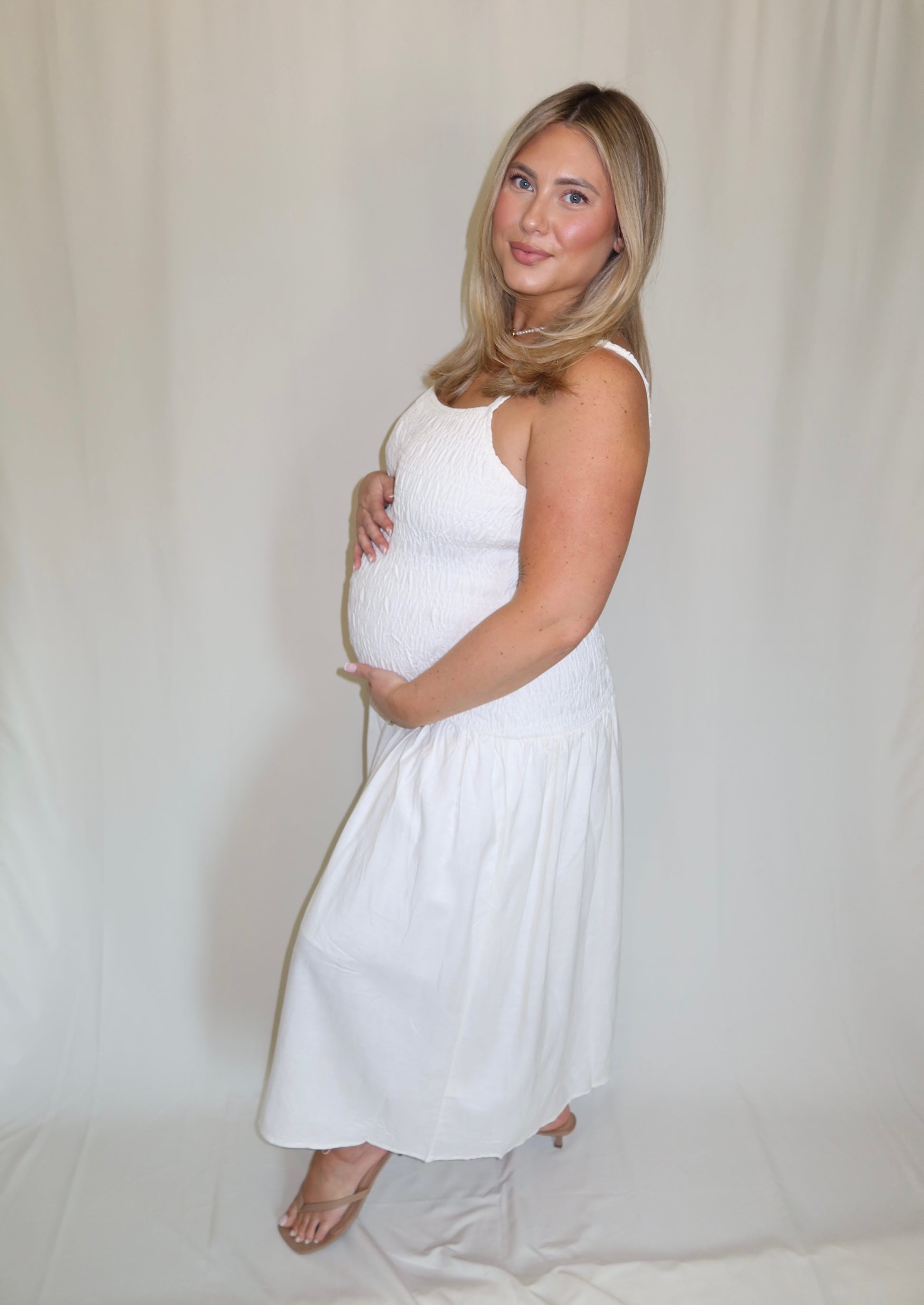Pregnant woman in a white dress standing against a plain background