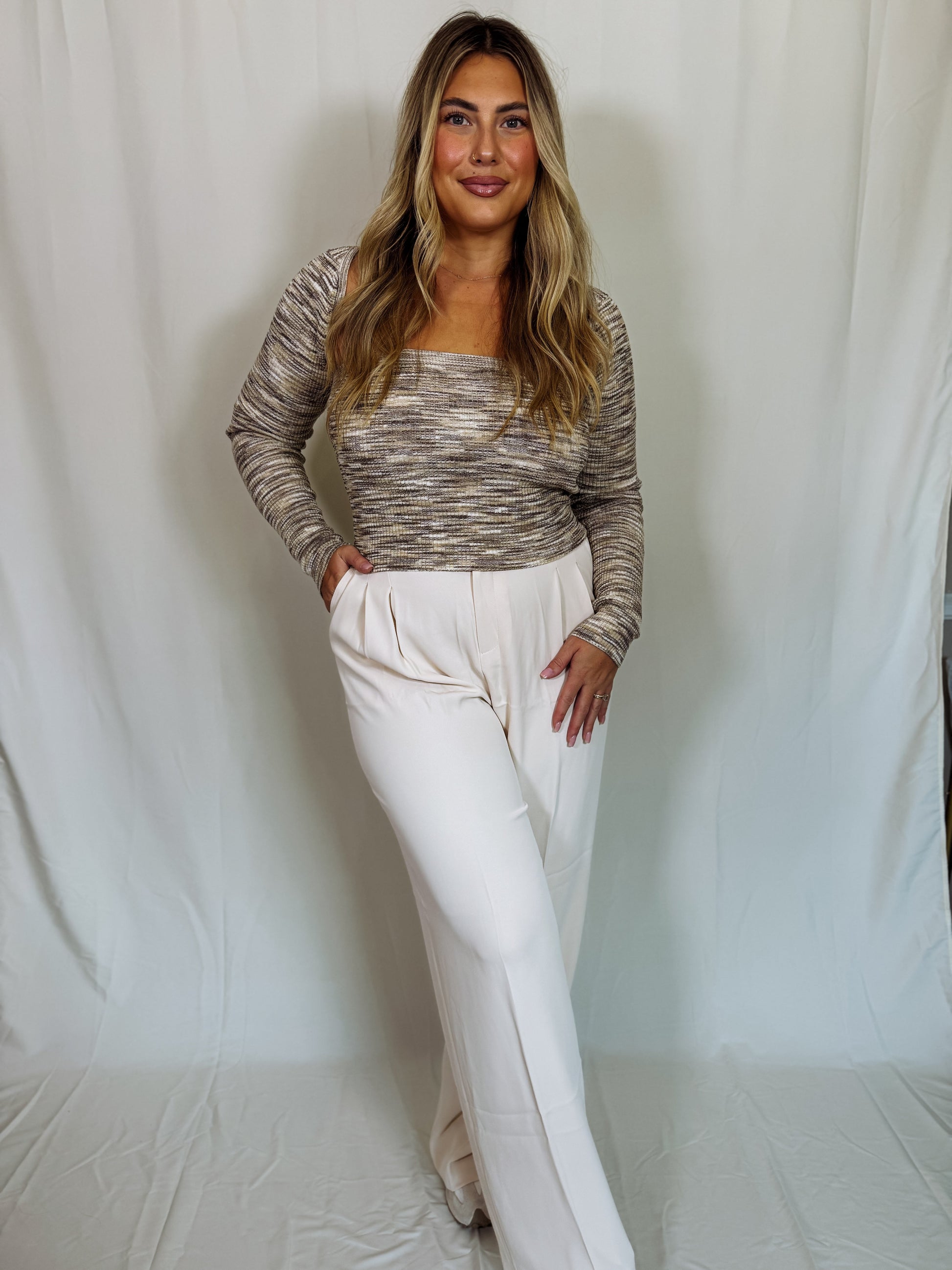 Woman wearing a patterned top and white pants against a plain background