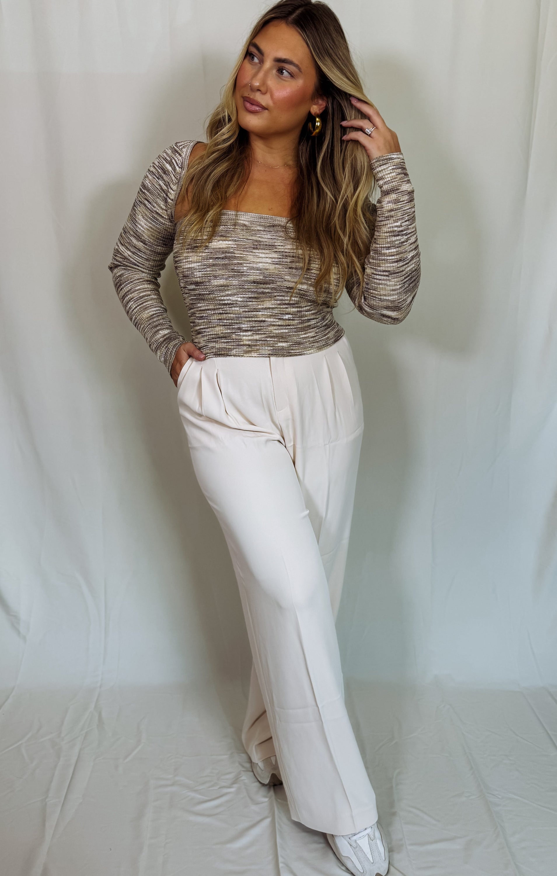 Woman wearing a patterned top and white pants against a plain background