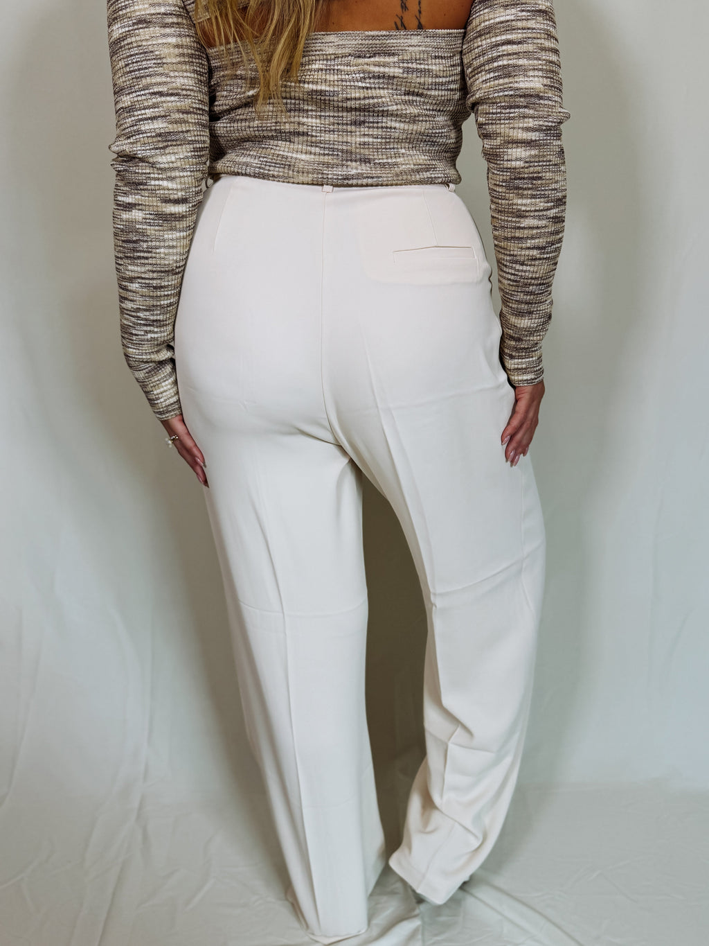 Person wearing a patterned long-sleeve top and white pants on a plain background