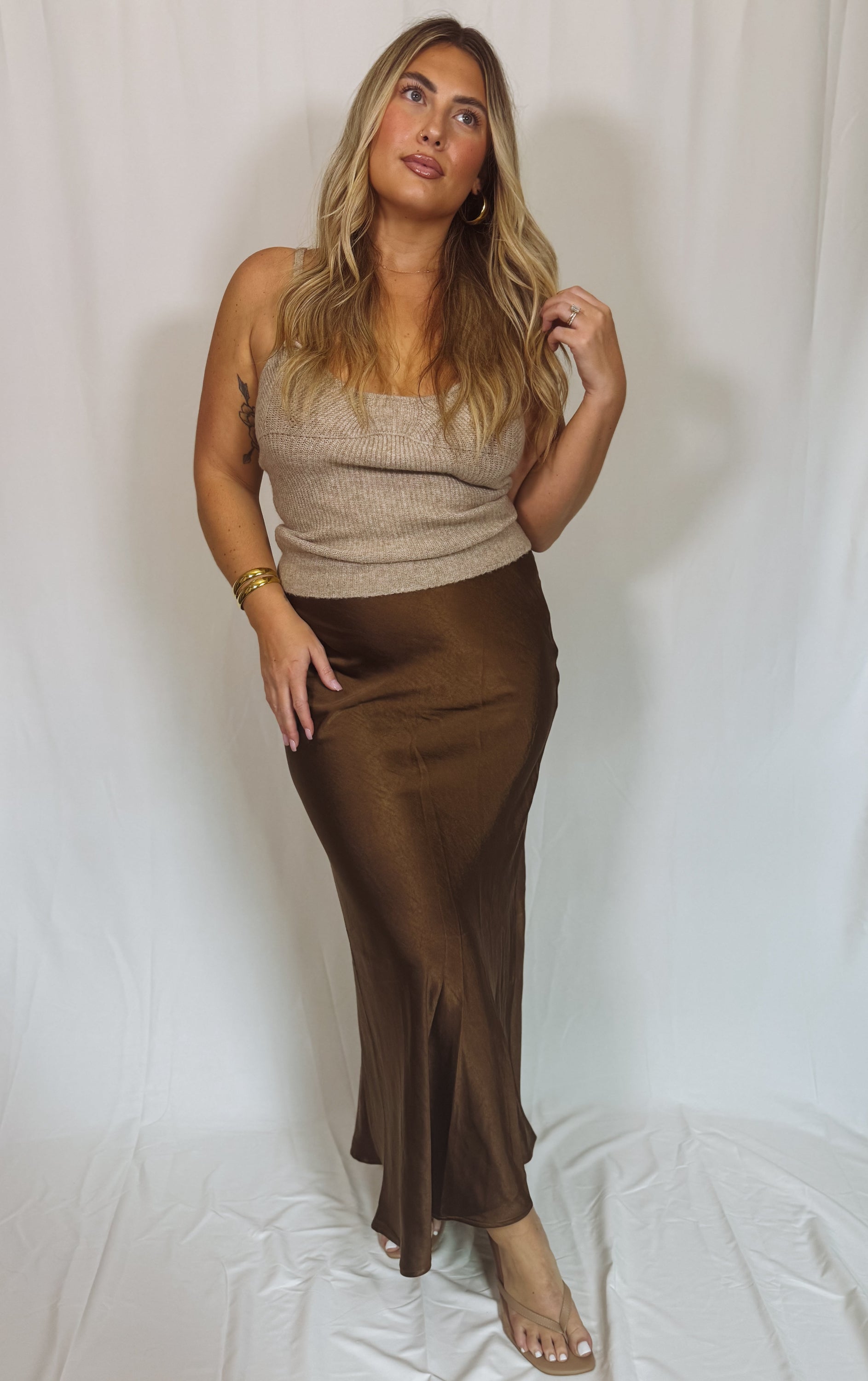 Woman wearing a beige top and brown skirt against a white background