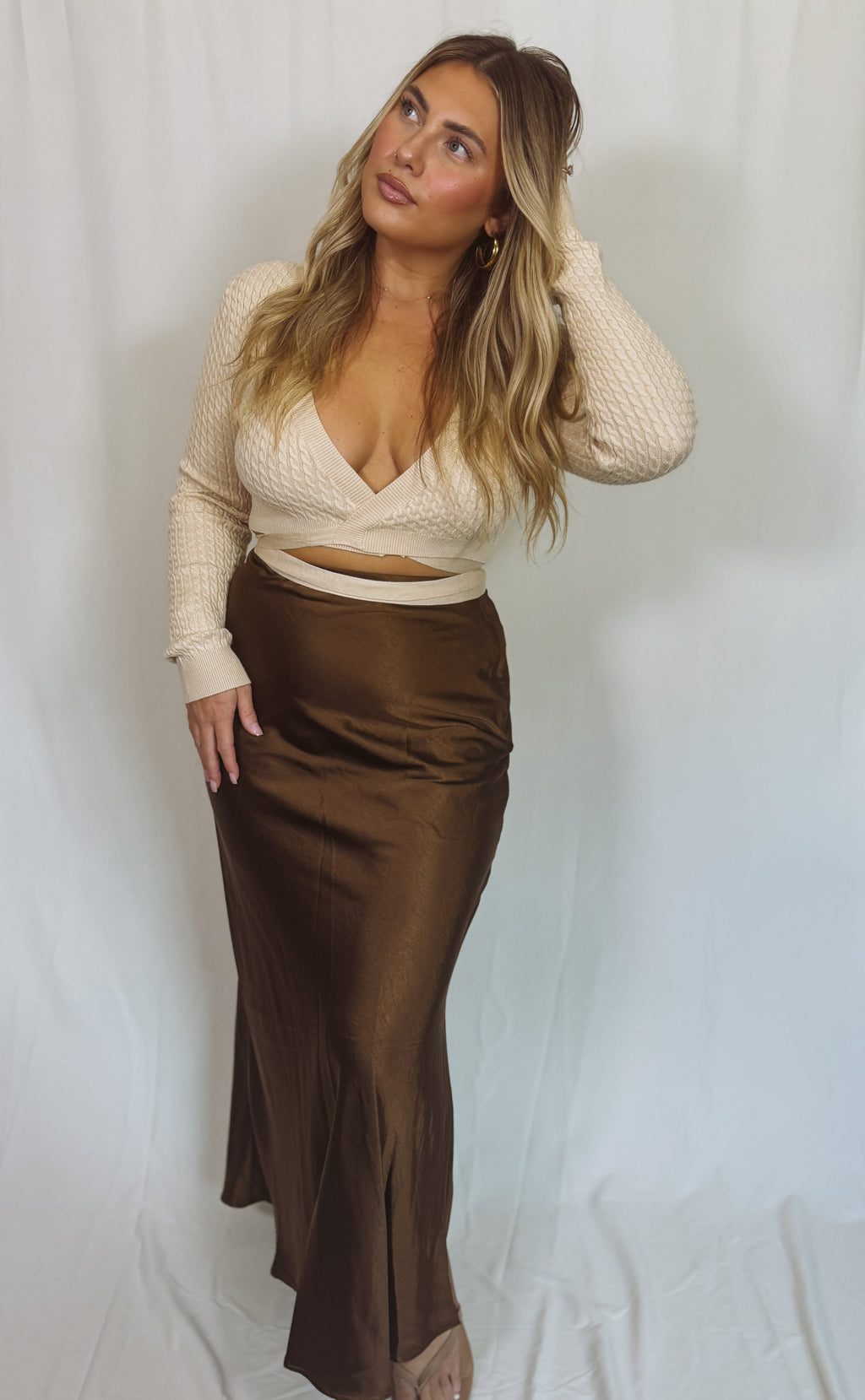 Woman wearing a cream wrap sweater and brown skirt against a white background