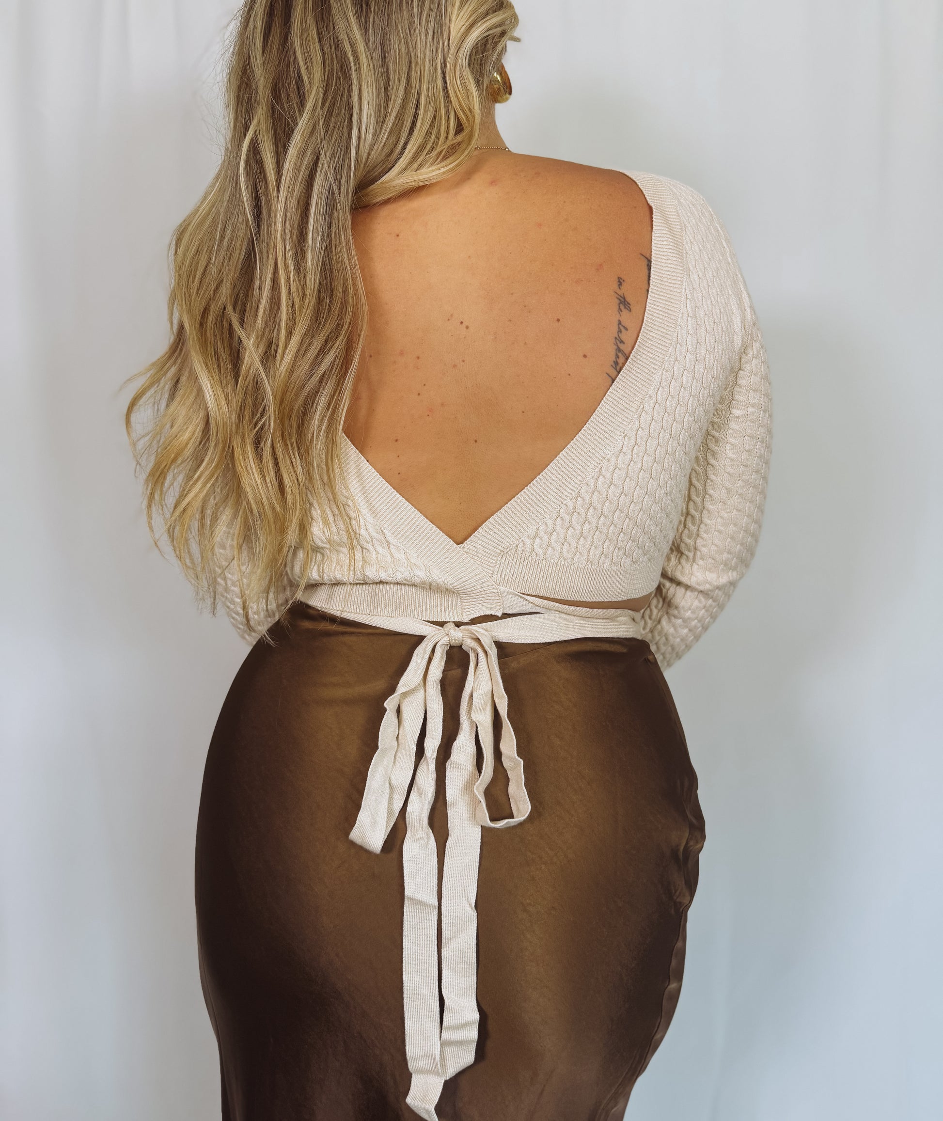 Woman wearing a cream sweater and brown skirt with a white background