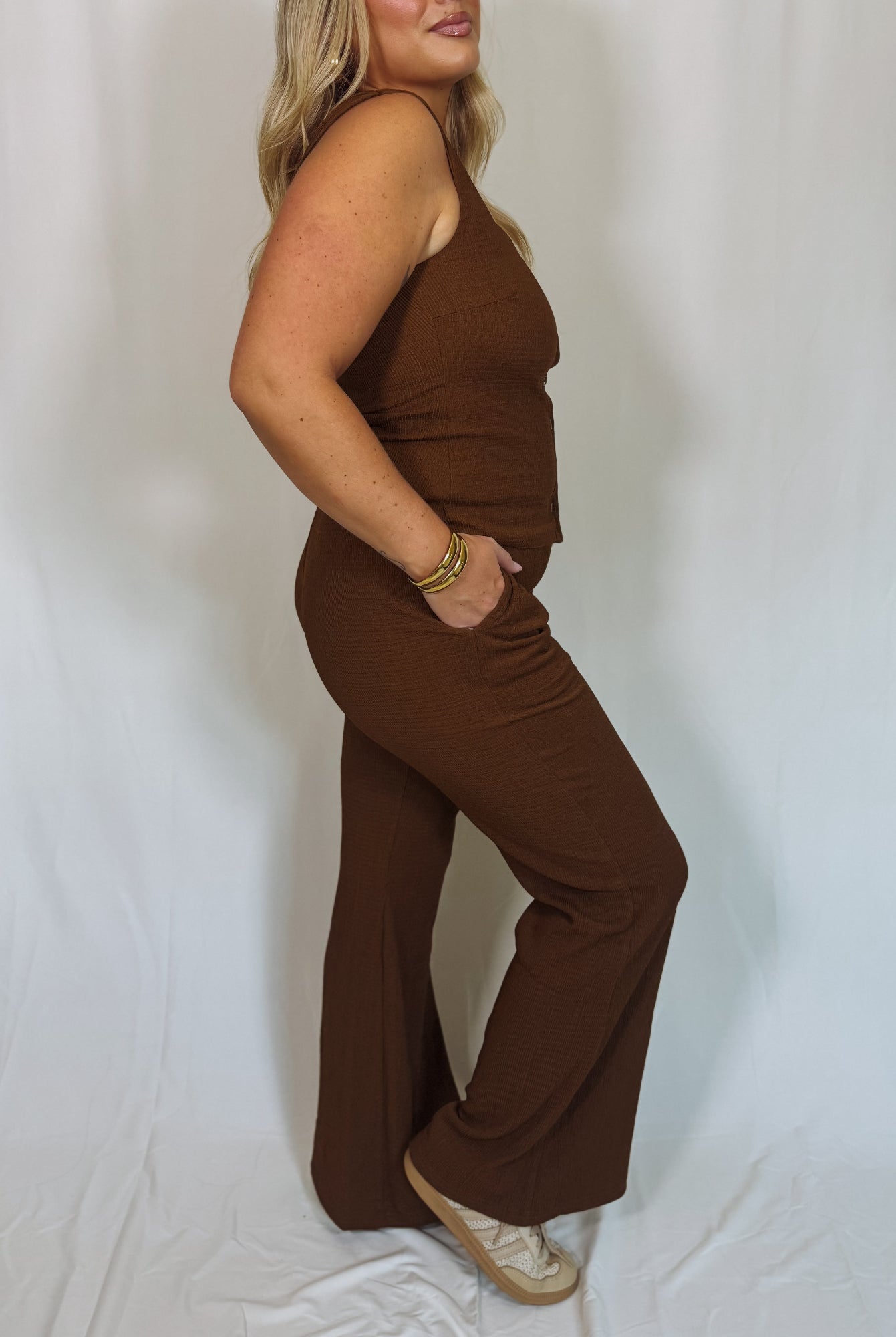 Woman wearing a brown sleeveless top and wide-leg pants against a white background