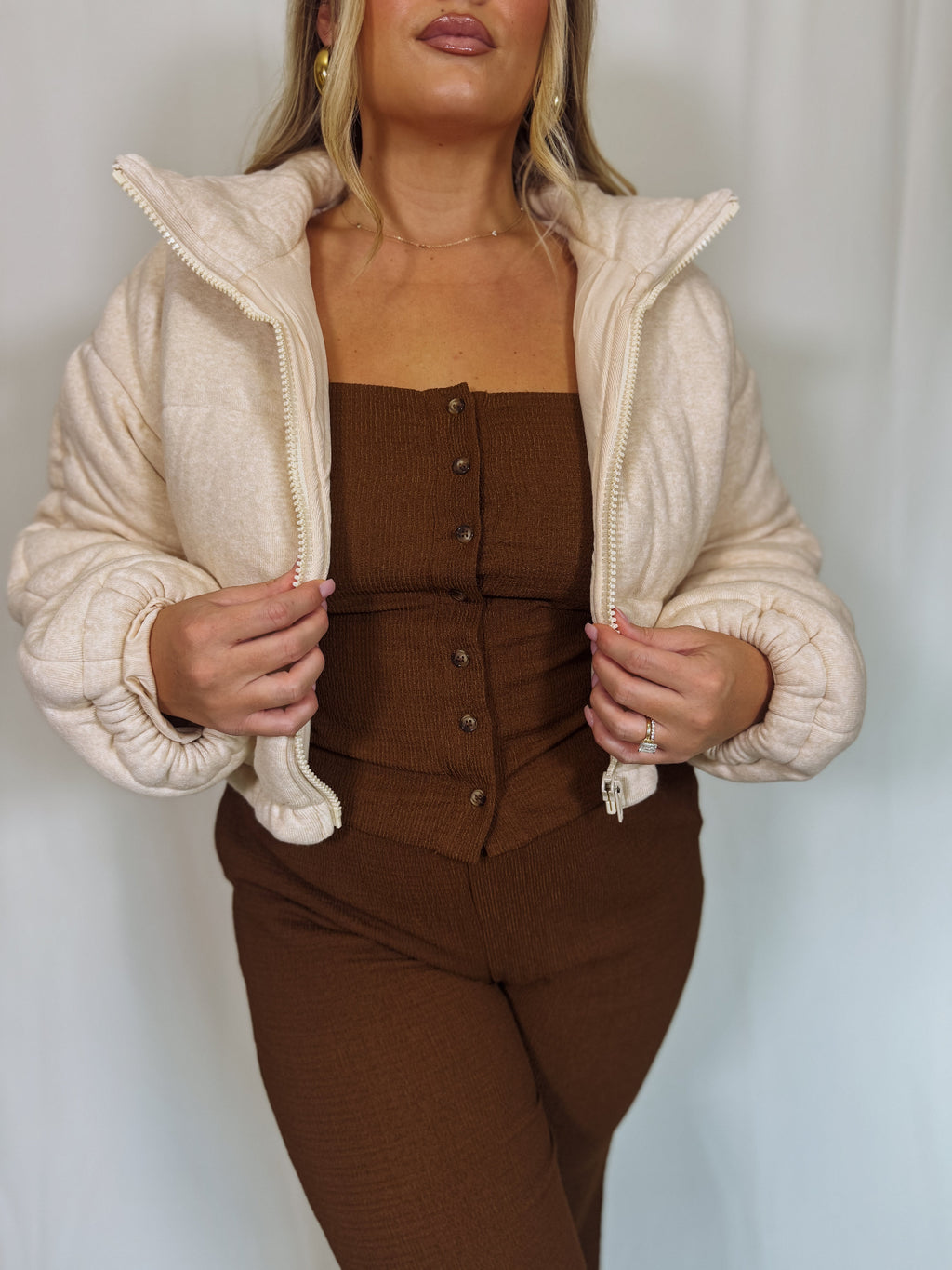 Woman wearing a beige puffer jacket over a brown outfit against a white background
