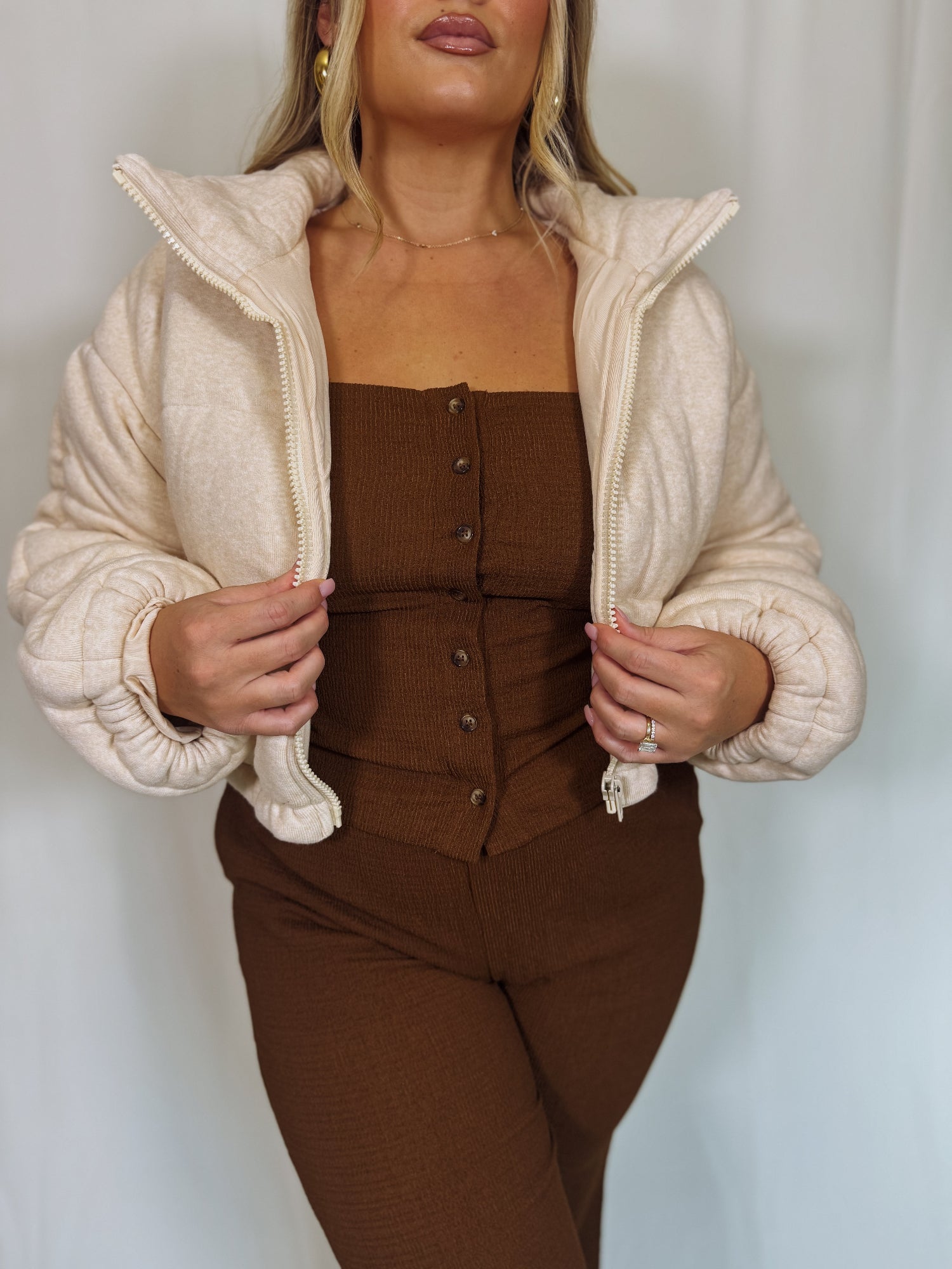 Woman wearing a beige puffer jacket over a brown outfit against a white background