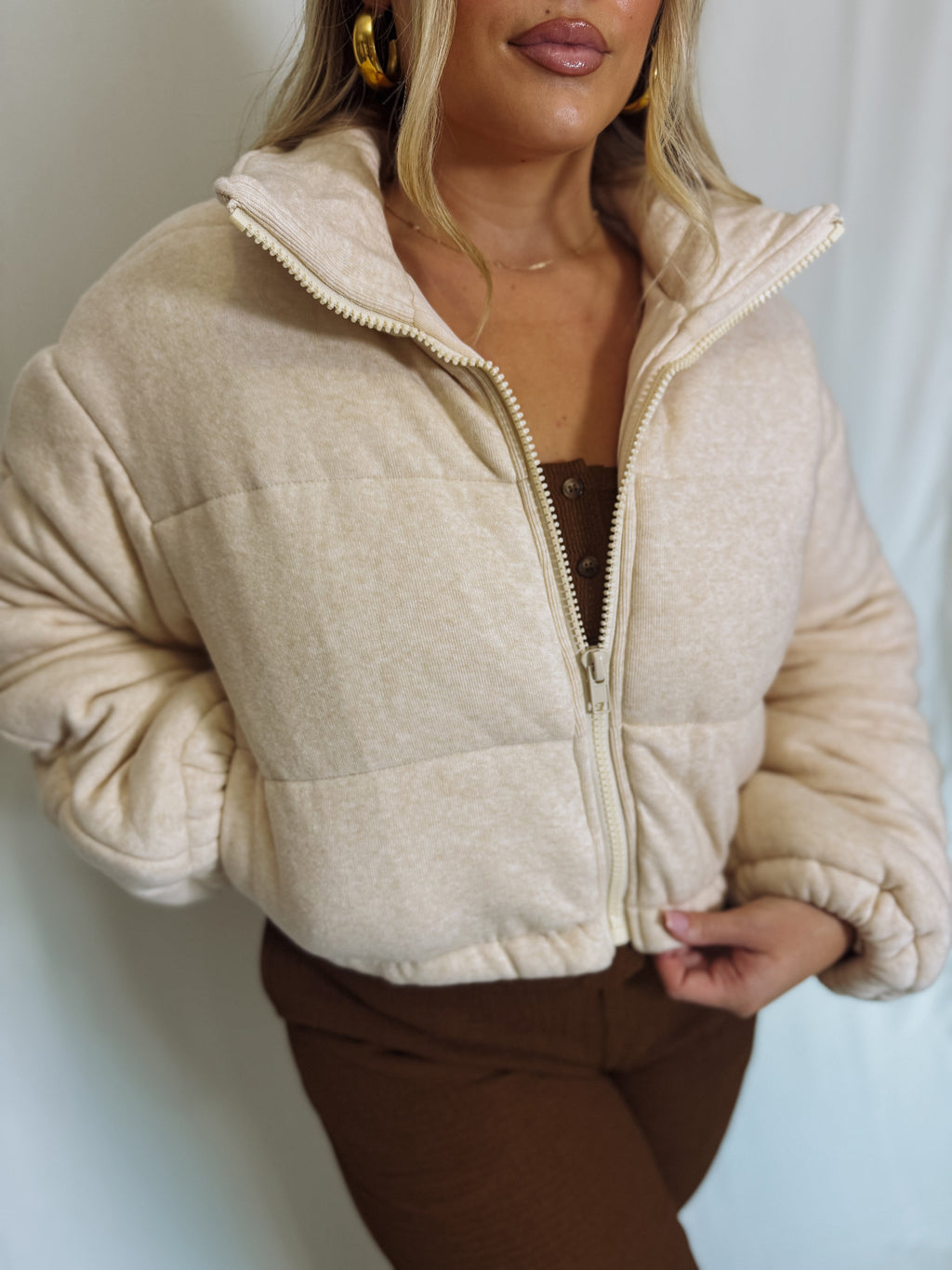 Woman wearing a beige puffer jacket against a plain background