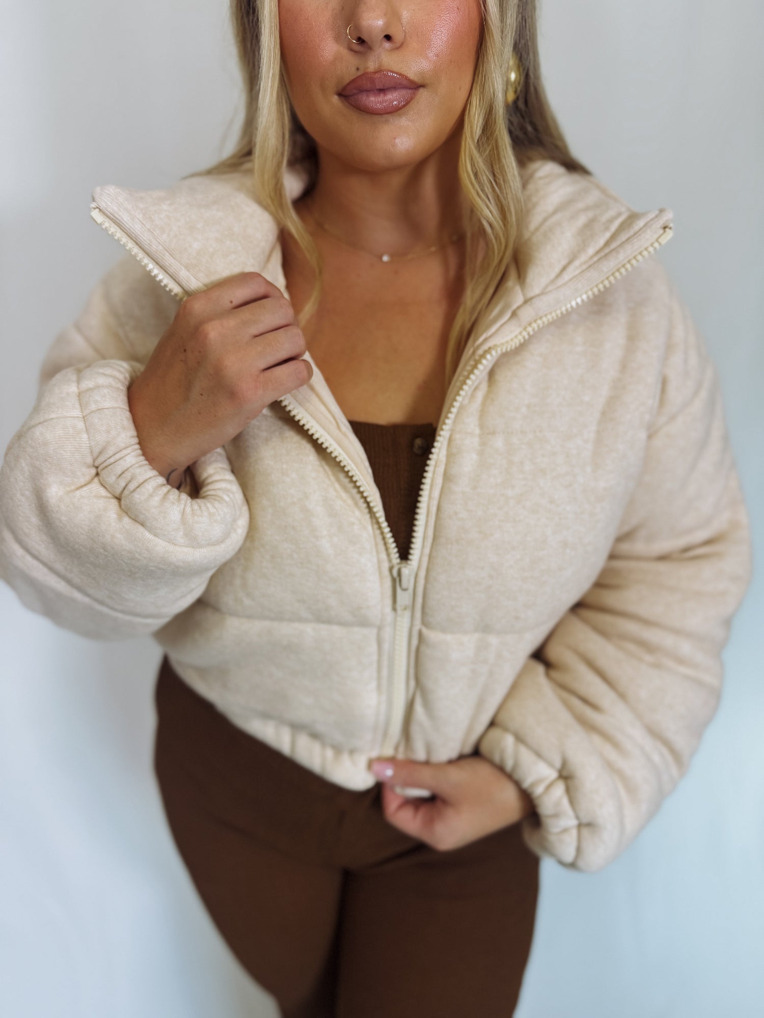 Woman wearing a beige puffer jacket over a brown outfit against a white background