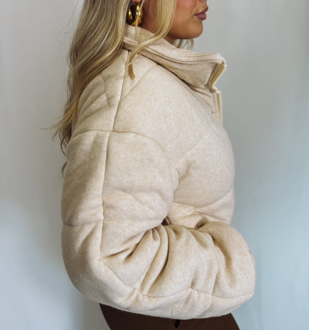 Person wearing a beige puffer jacket against a plain background