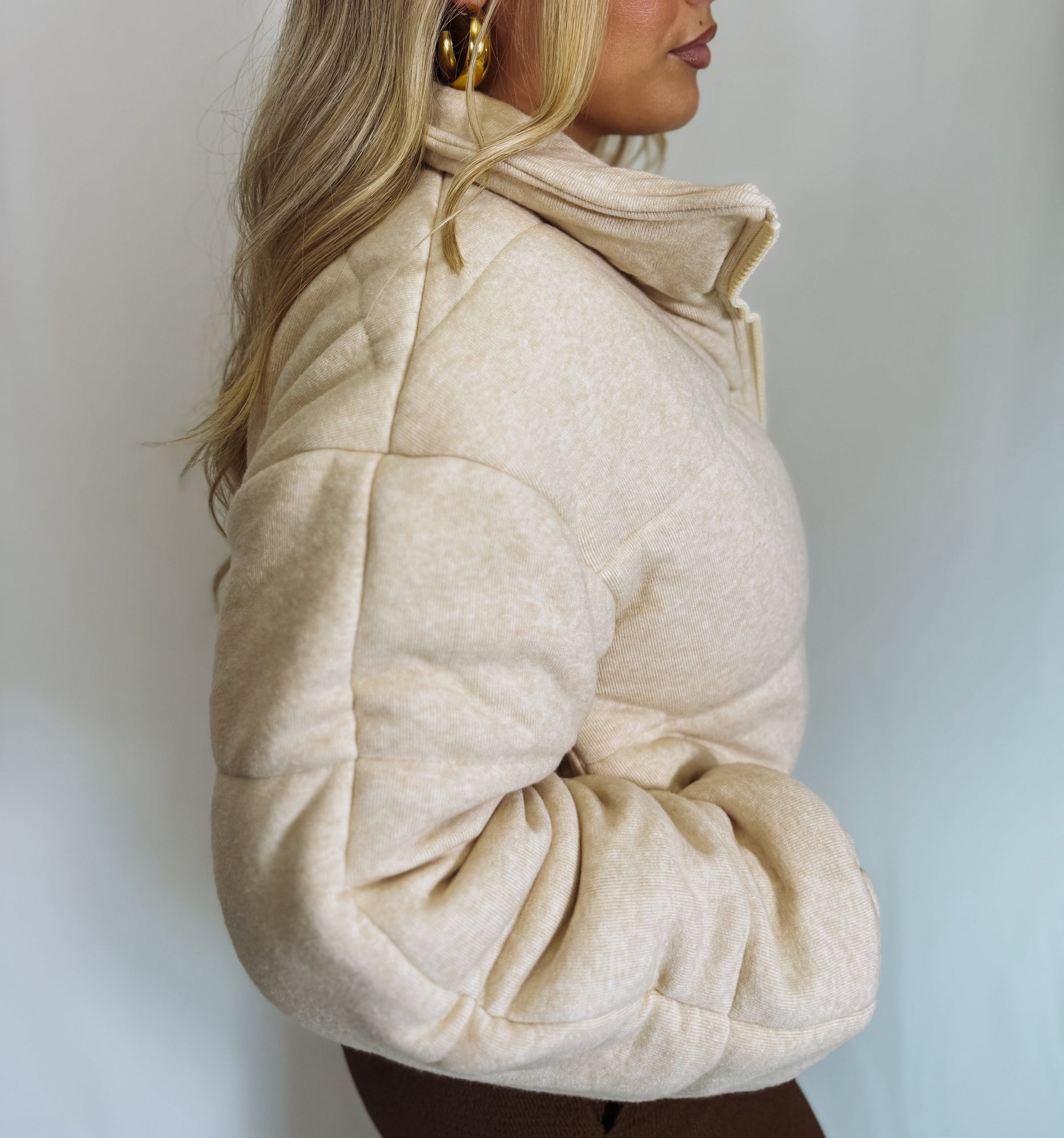 Person wearing a beige puffer jacket against a plain background