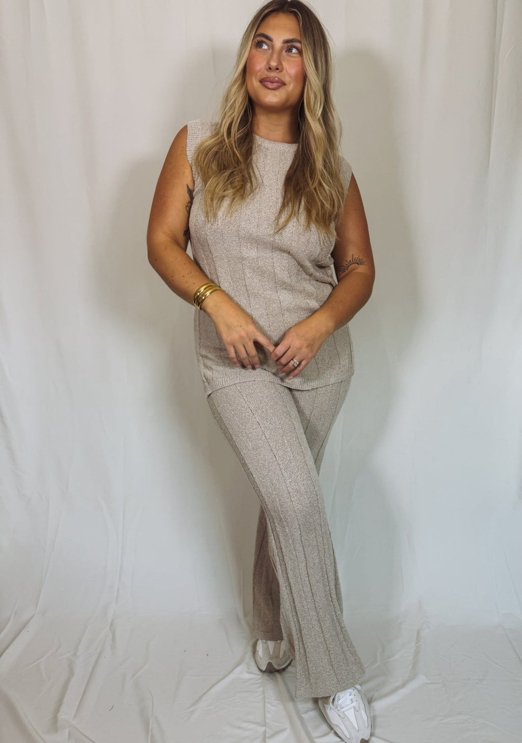 Woman wearing a beige sleeveless top and pants against a plain background