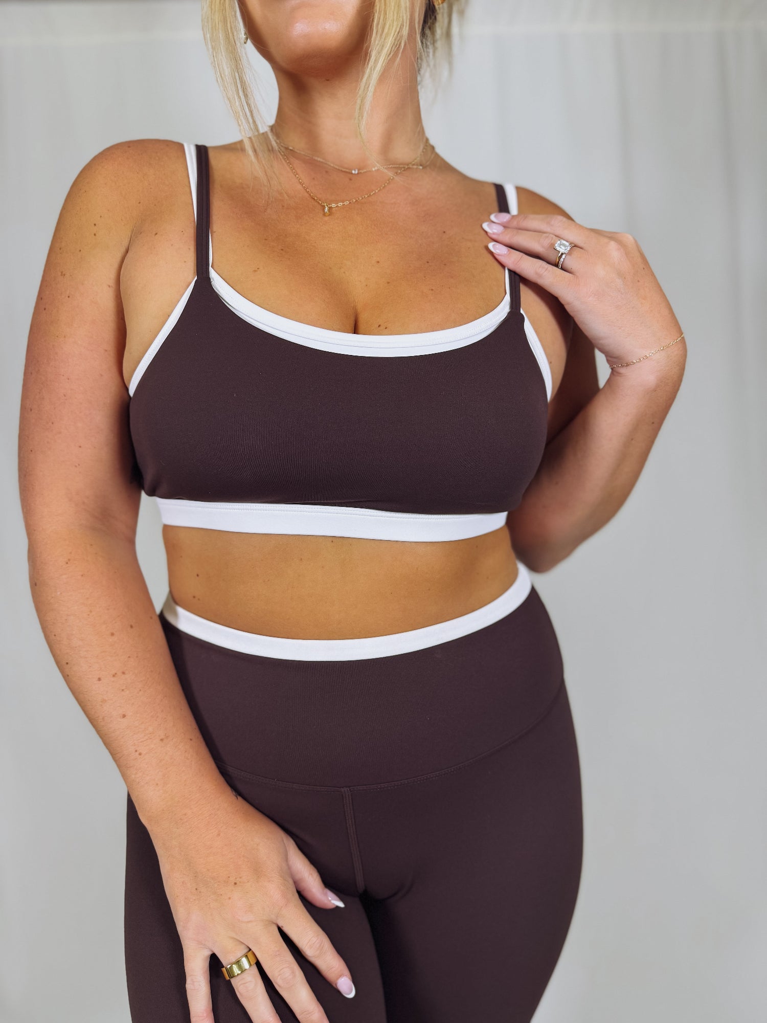 Person wearing a brown sports bra and leggings set with white accents on a plain background