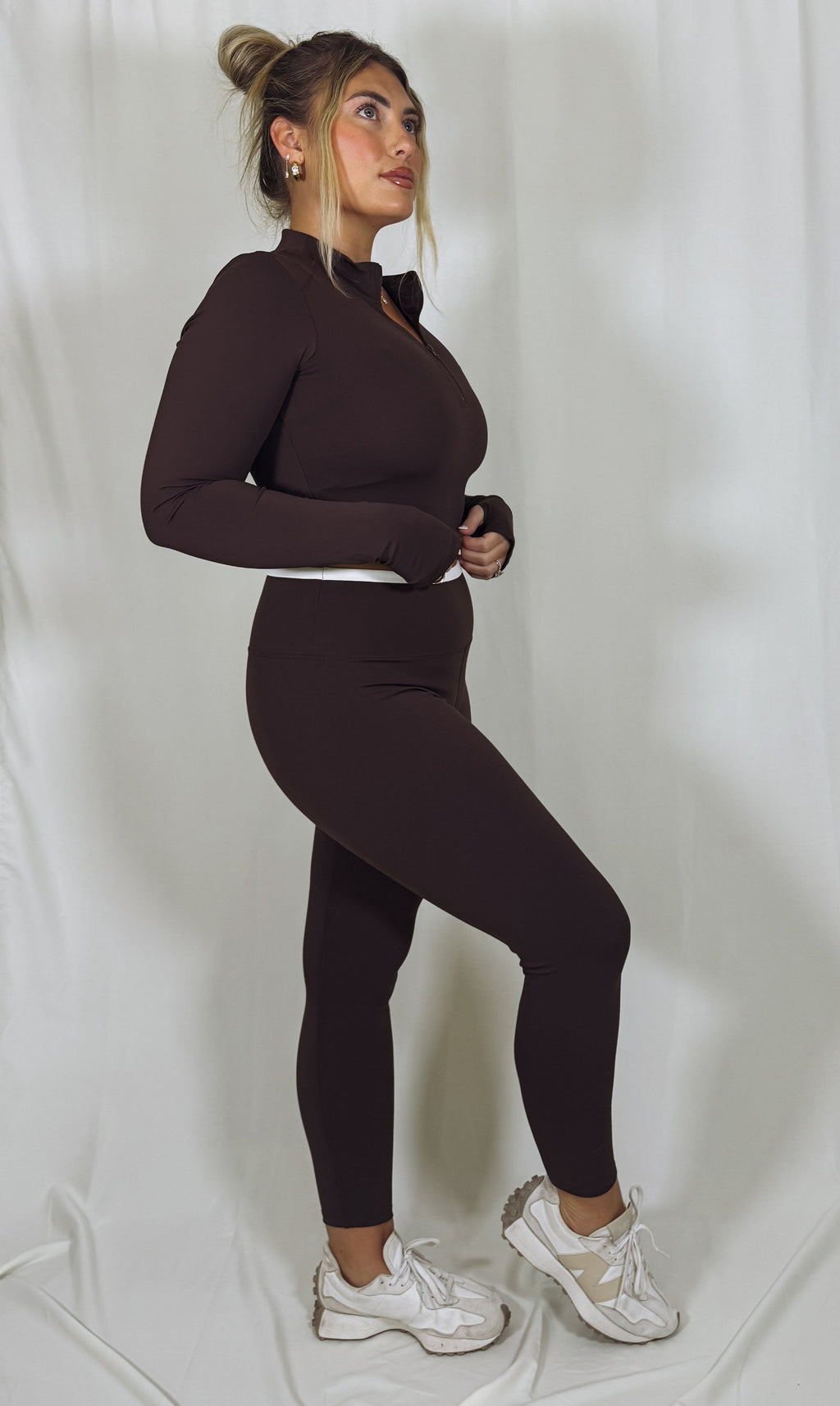 Woman wearing a brown outfit with white sneakers on a plain background