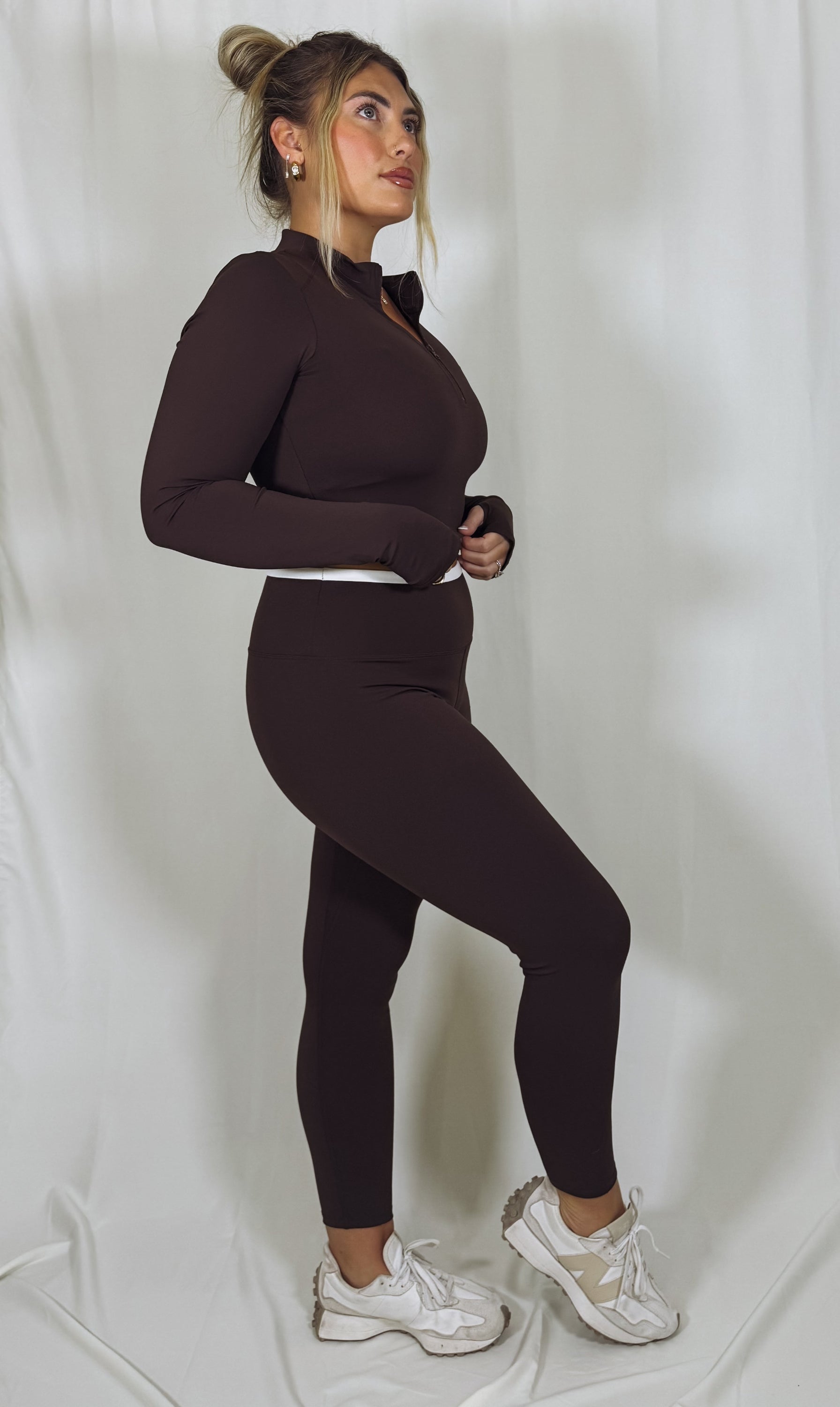 Woman wearing a brown outfit with white sneakers on a plain background