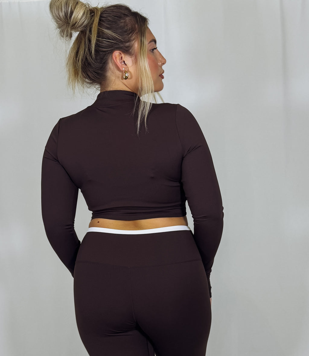 Woman wearing a dark brown long-sleeve crop top and leggings against a plain background