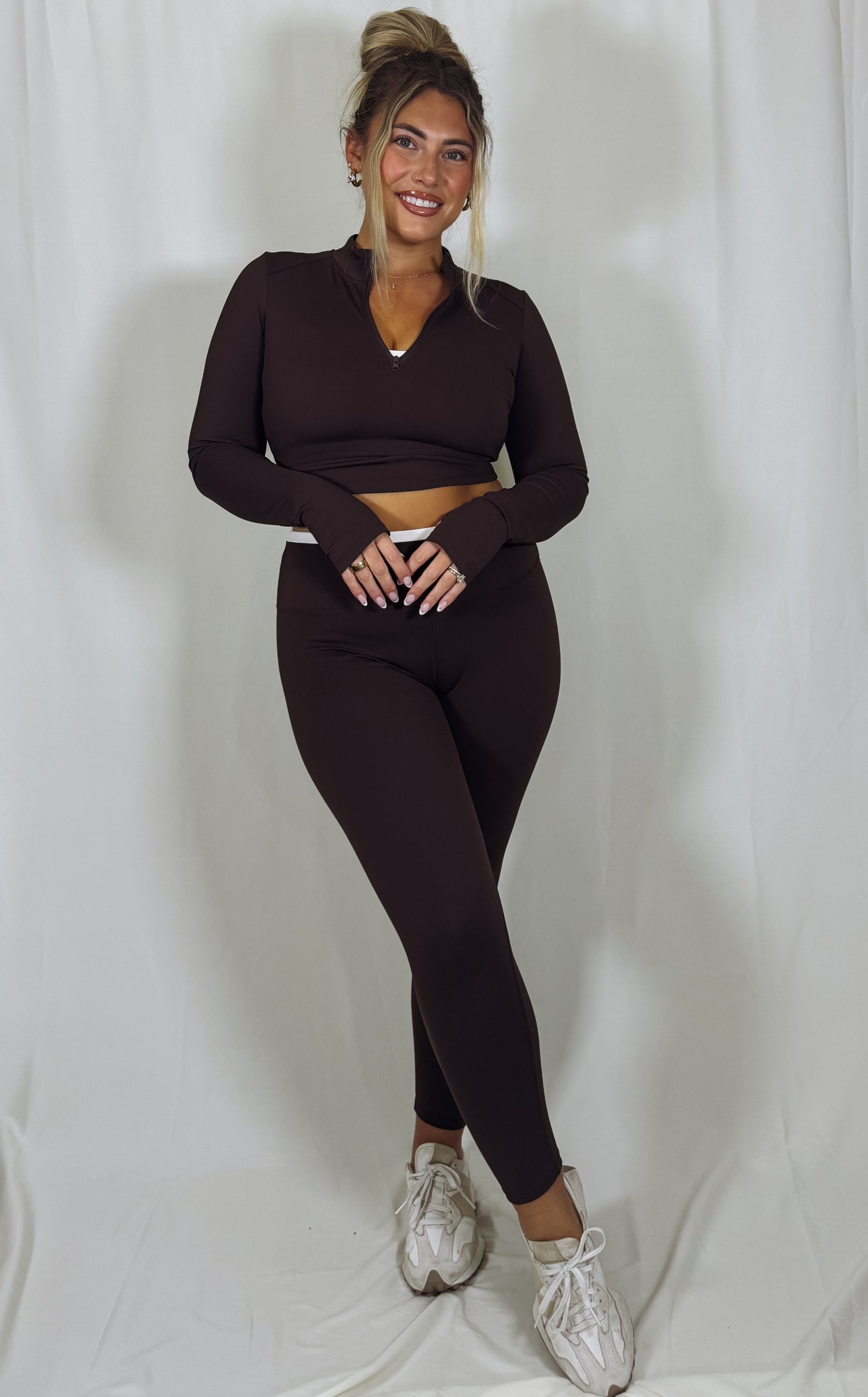Woman wearing a dark brown long-sleeve top and leggings set on a white background