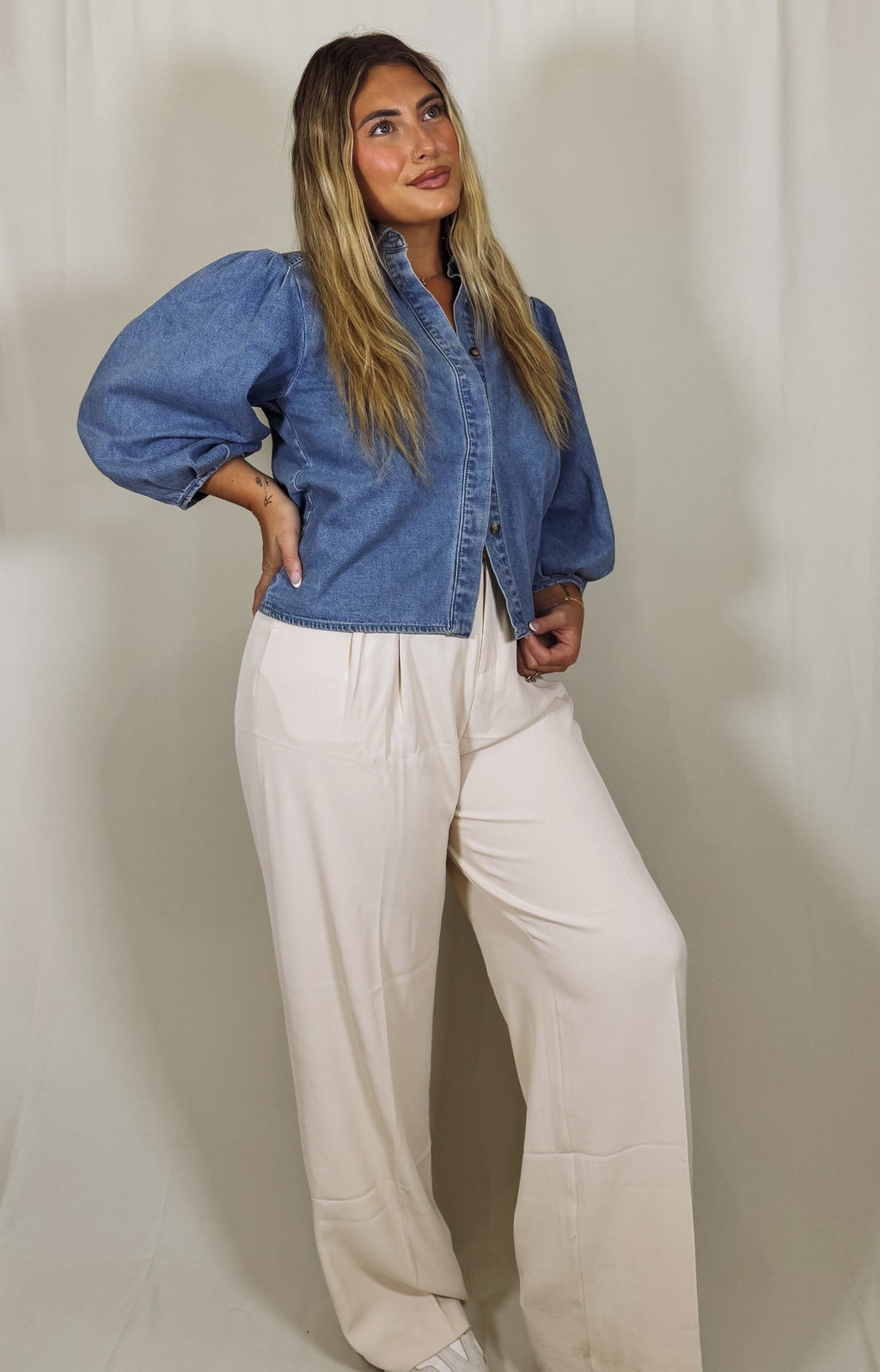 Person wearing a blue denim shirt and white pants against a plain background