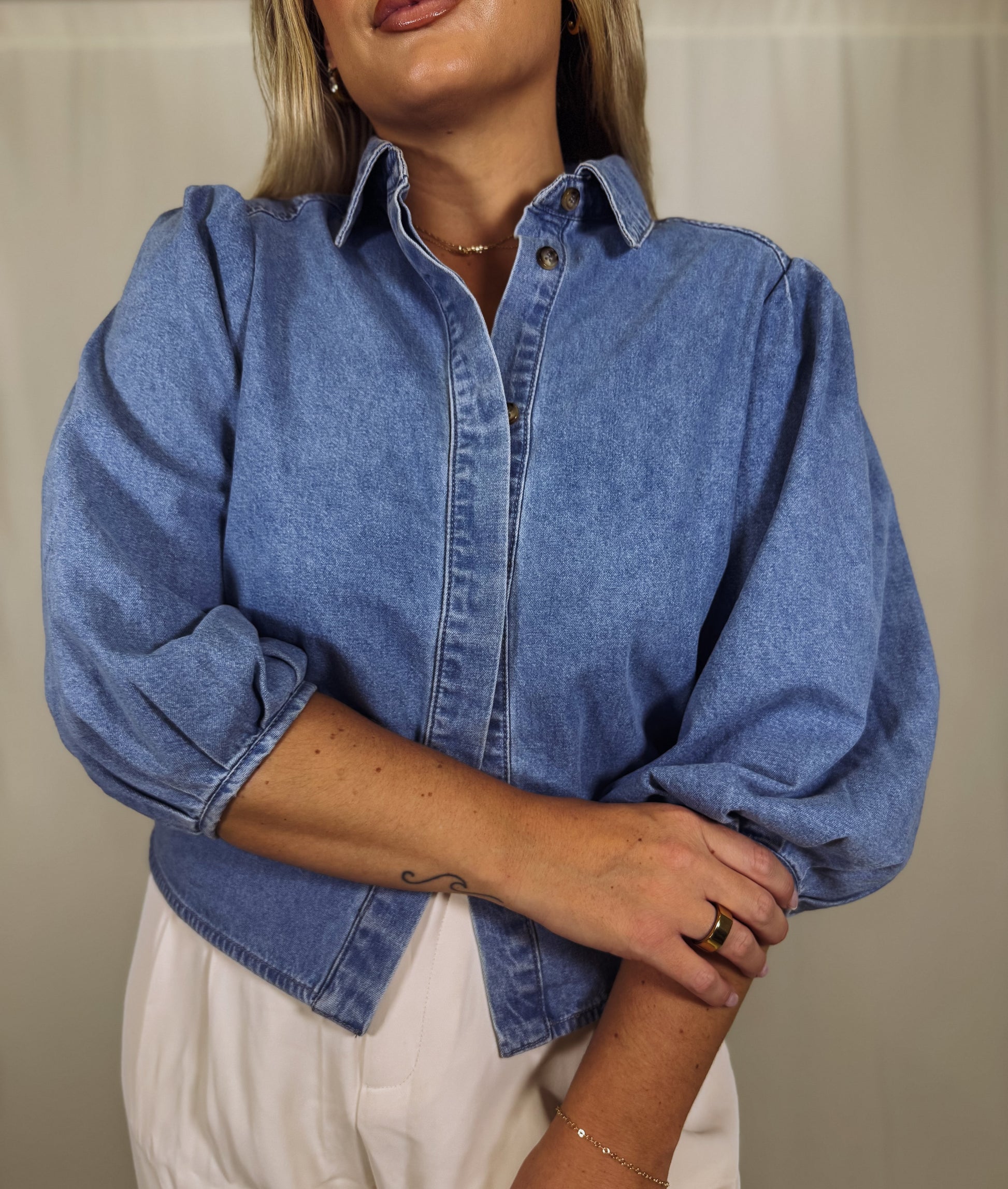 Person wearing a blue denim shirt with puff sleeves against a neutral background