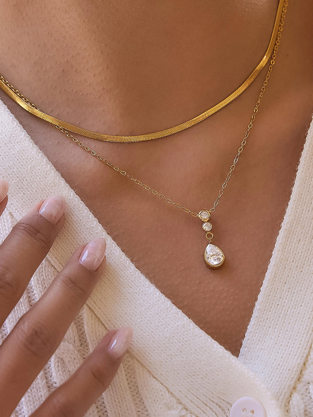 Gold necklace with a teardrop pendant worn by a person in a white top.