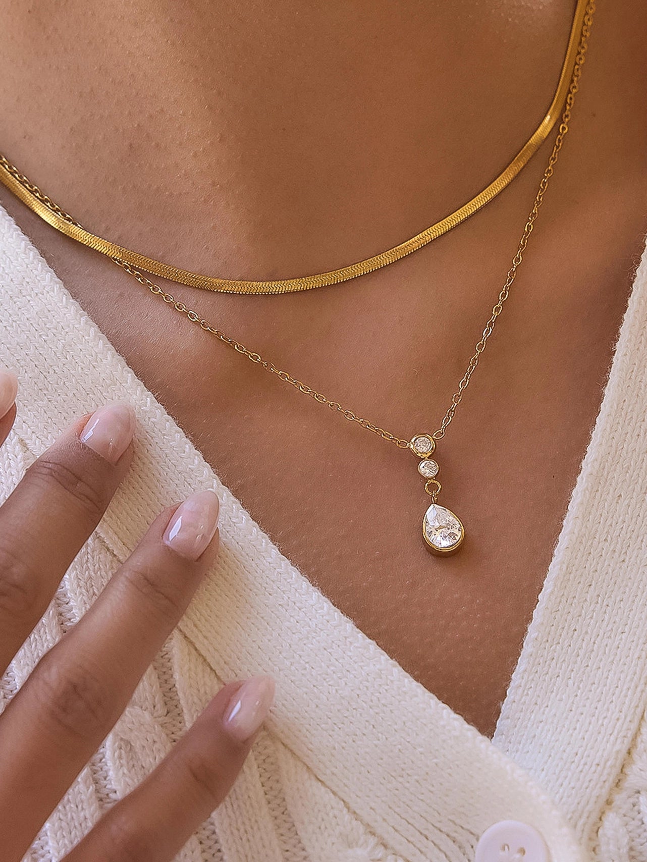 Gold necklace with a teardrop pendant worn by a person in a white top.