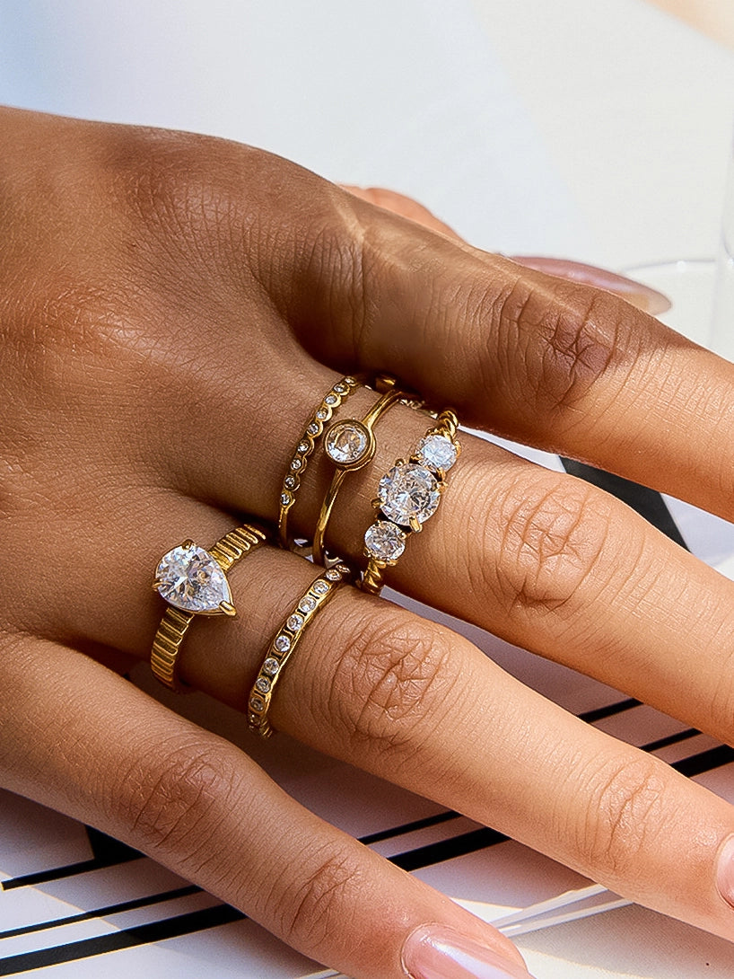 Hand wearing multiple gold rings with cz accents on a light background
